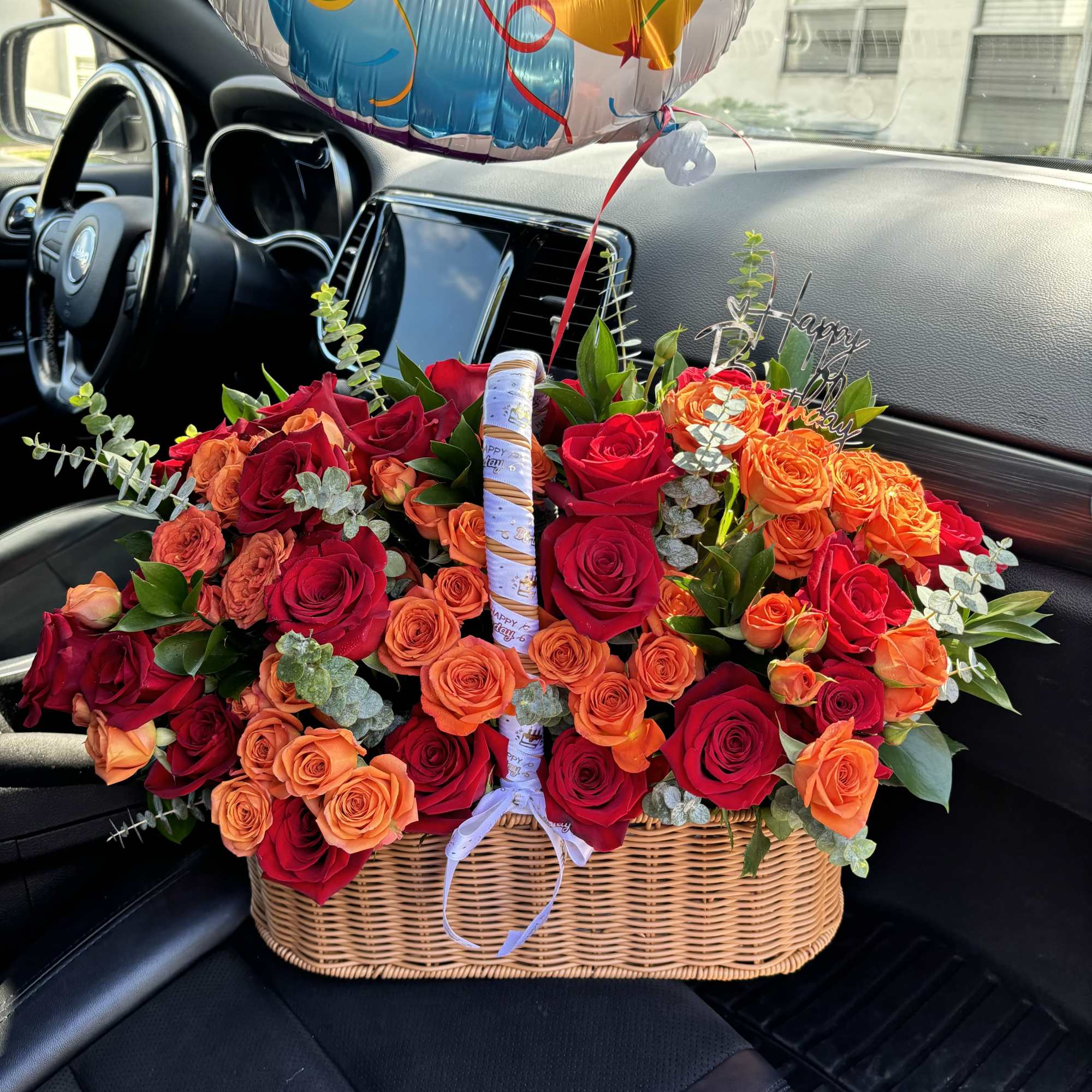 Basket of red and orange roses with a birthday balloon in a car