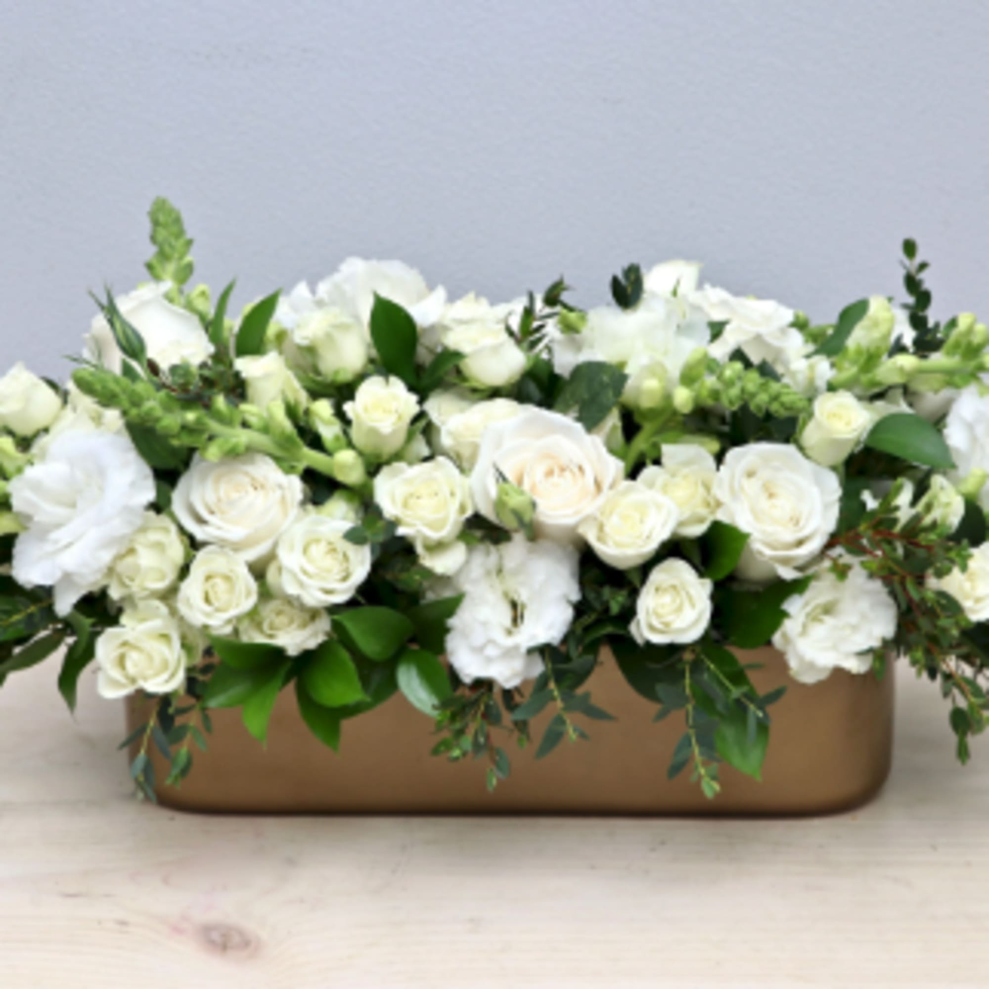 Long low arrangement of white roses and snapdragons in a gold rectangular container