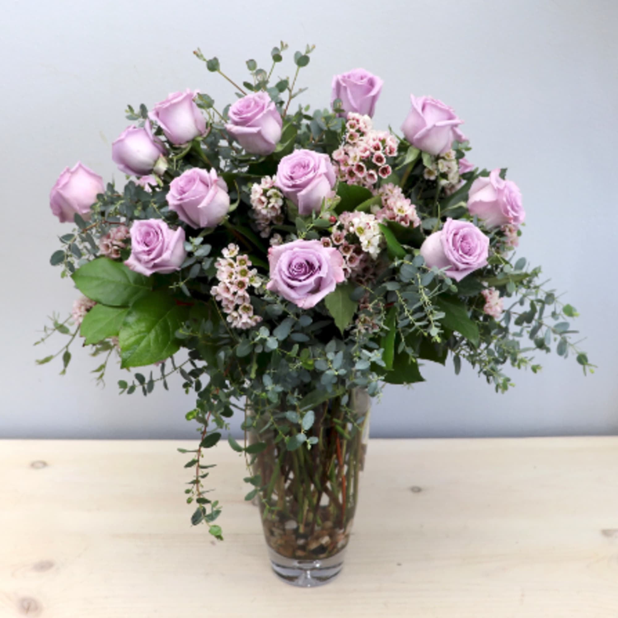 Tall arrangement of lavender roses with small pink blooms in a clear glass vase