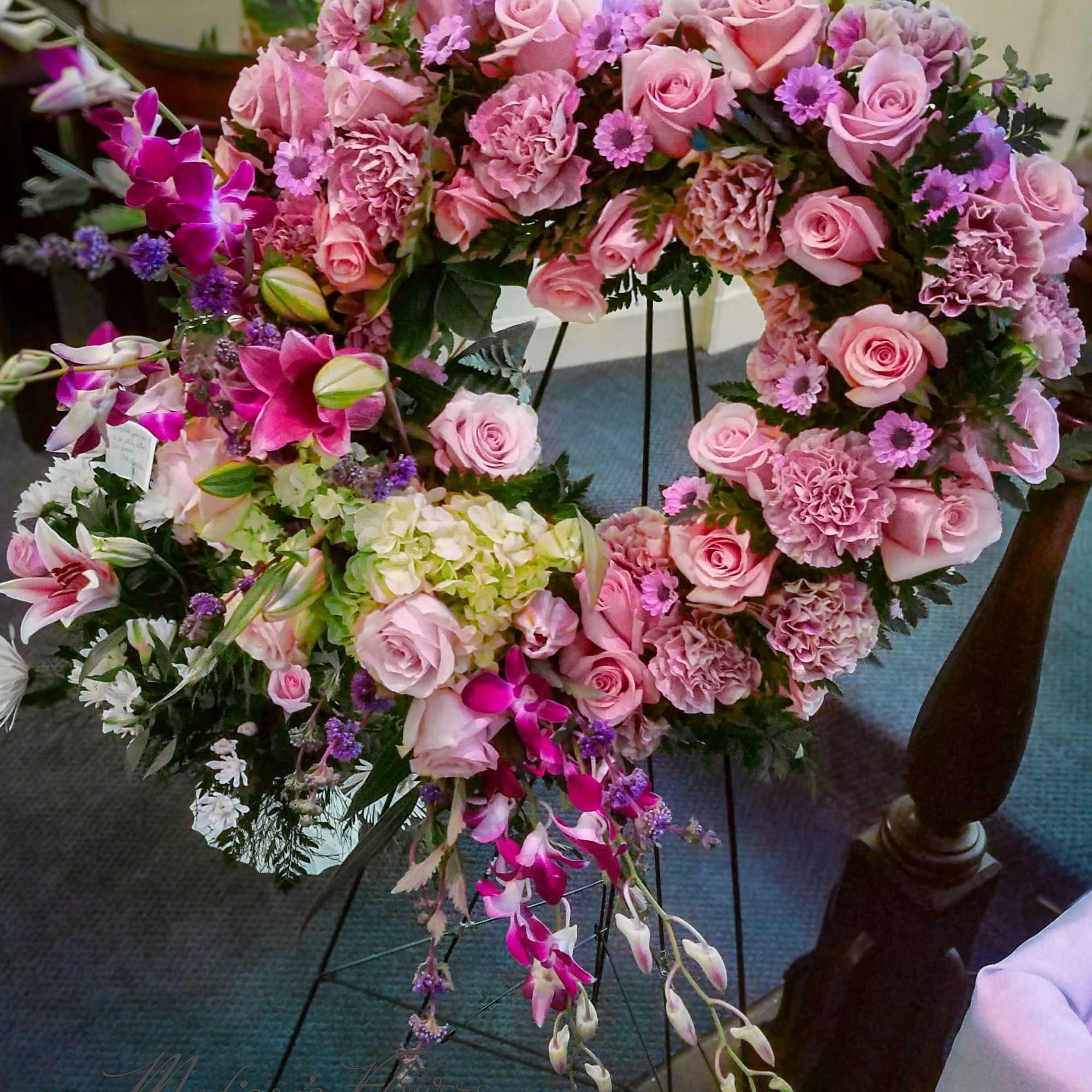 Tall pink and purple standing wreath of roses, carnations, lilies, and orchids on an easel