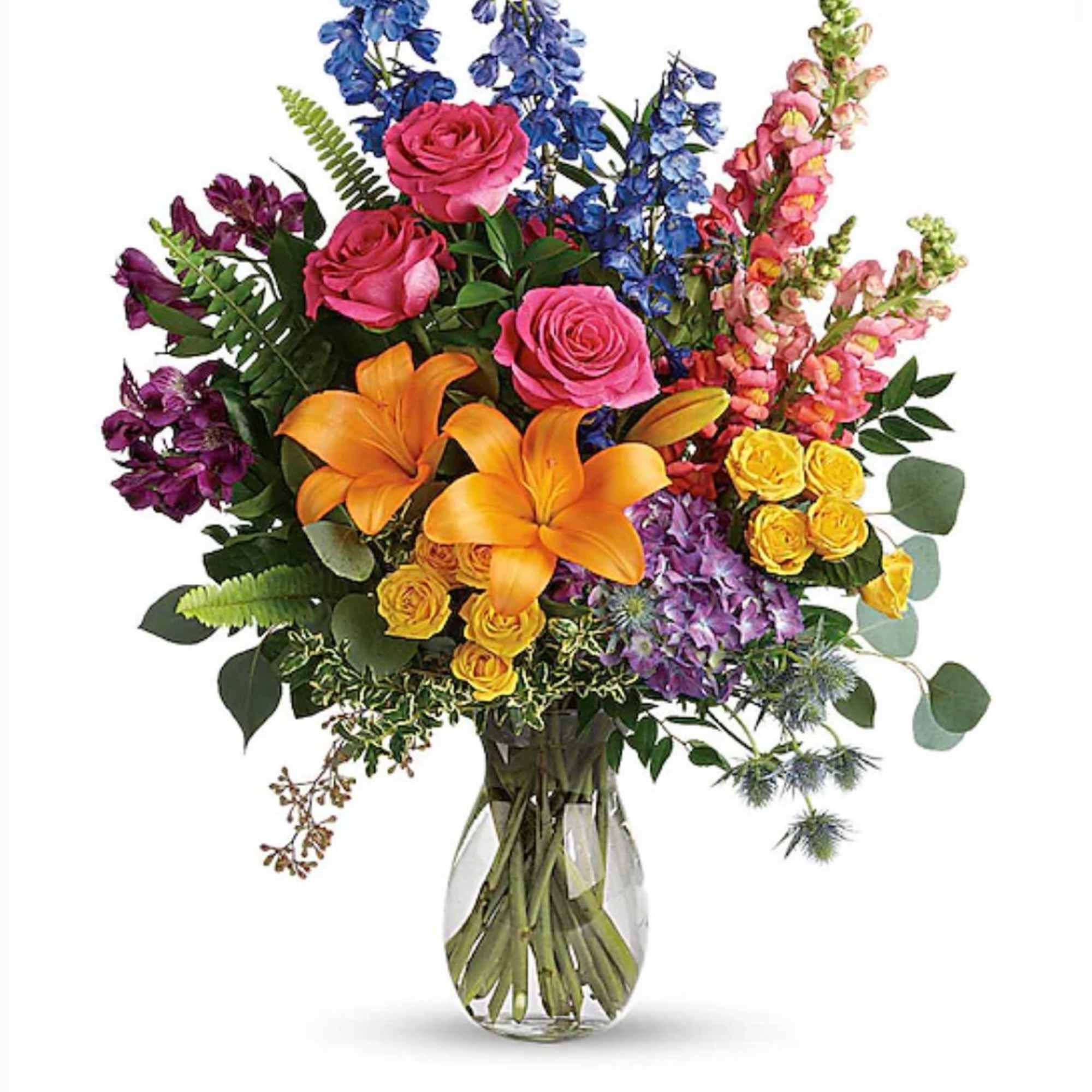 Tall mixed bouquet of pink roses, orange lilies, blue delphinium and yellow blooms in a clear glass vase