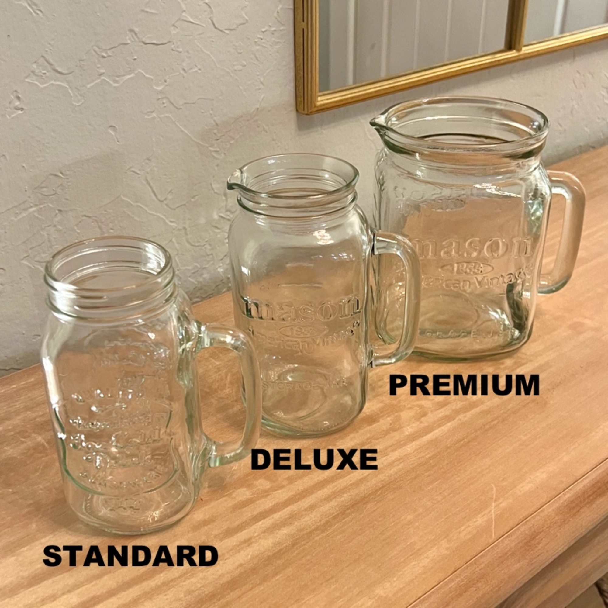 Three clear mason jar-style pitchers in small, medium, and large sizes on a wooden surface