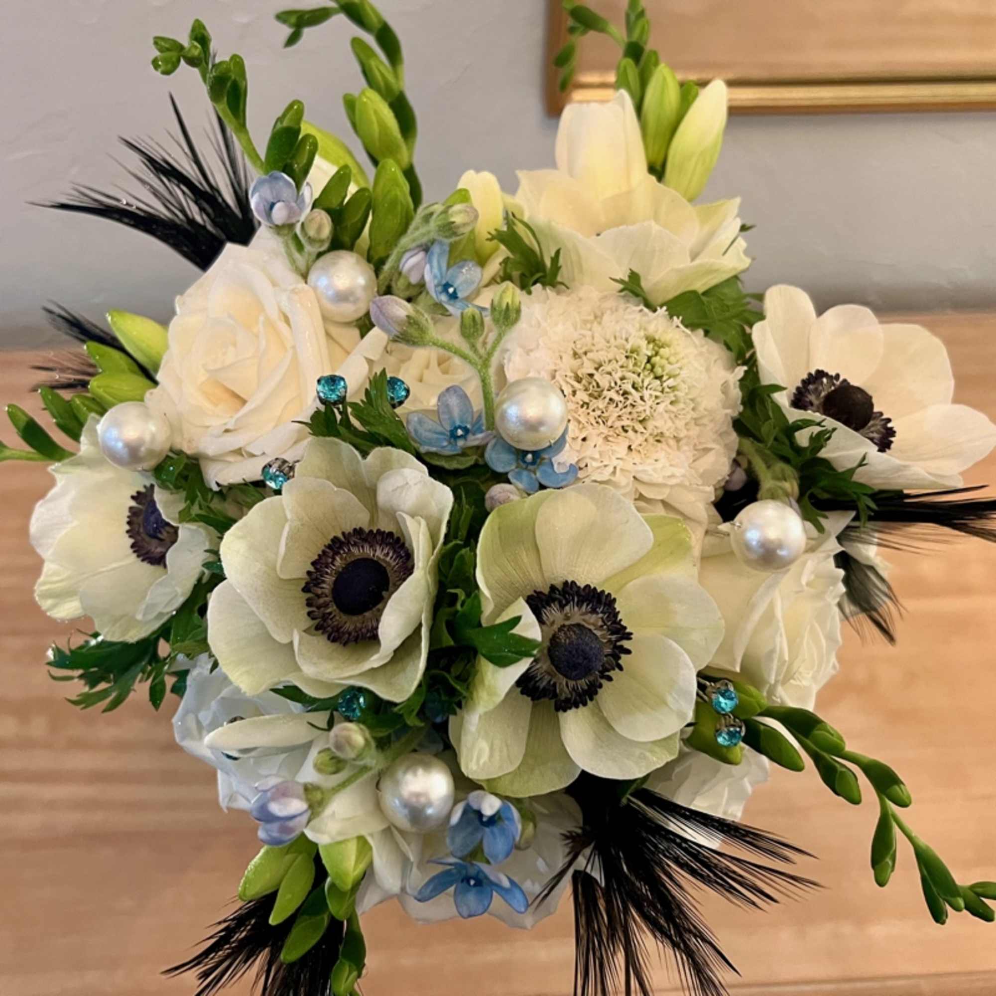 Compact bouquet of white anemones and roses with blue blooms, pearl picks, and black accents.