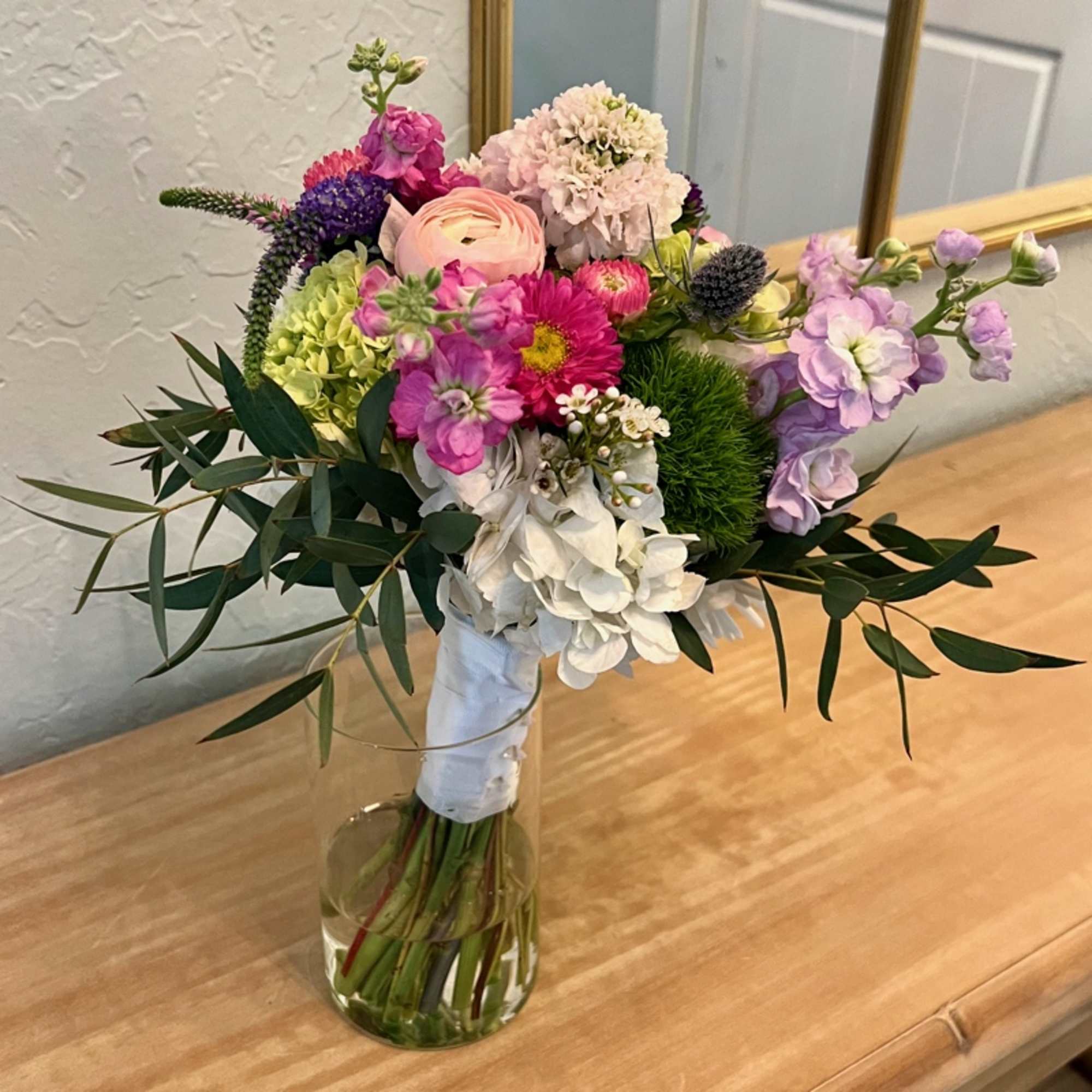 Hand-tied mixed bouquet of pink, white, and purple flowers in a clear glass vase