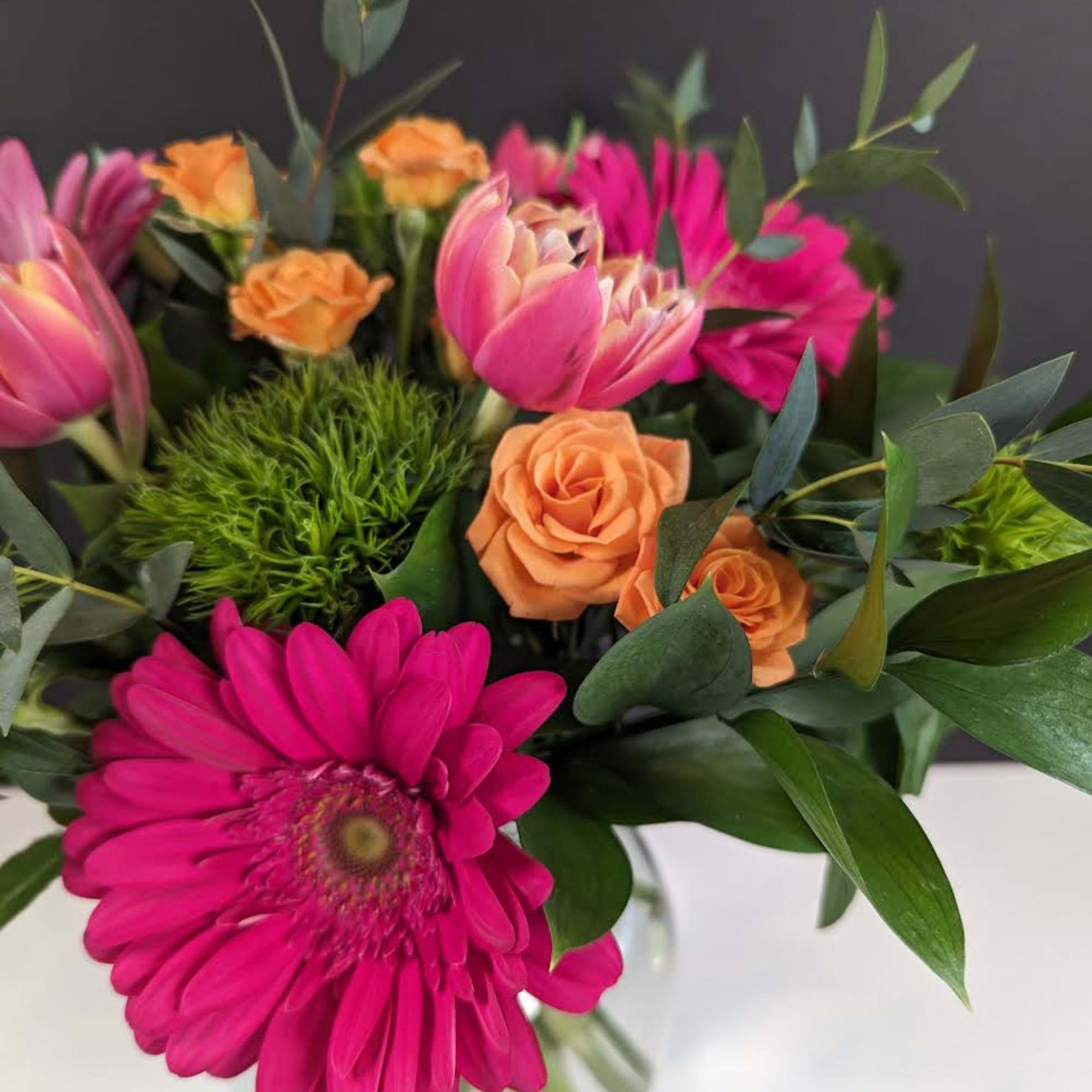 Bright bouquet of hot pink gerbera, pink tulips, and orange roses in a clear glass vase