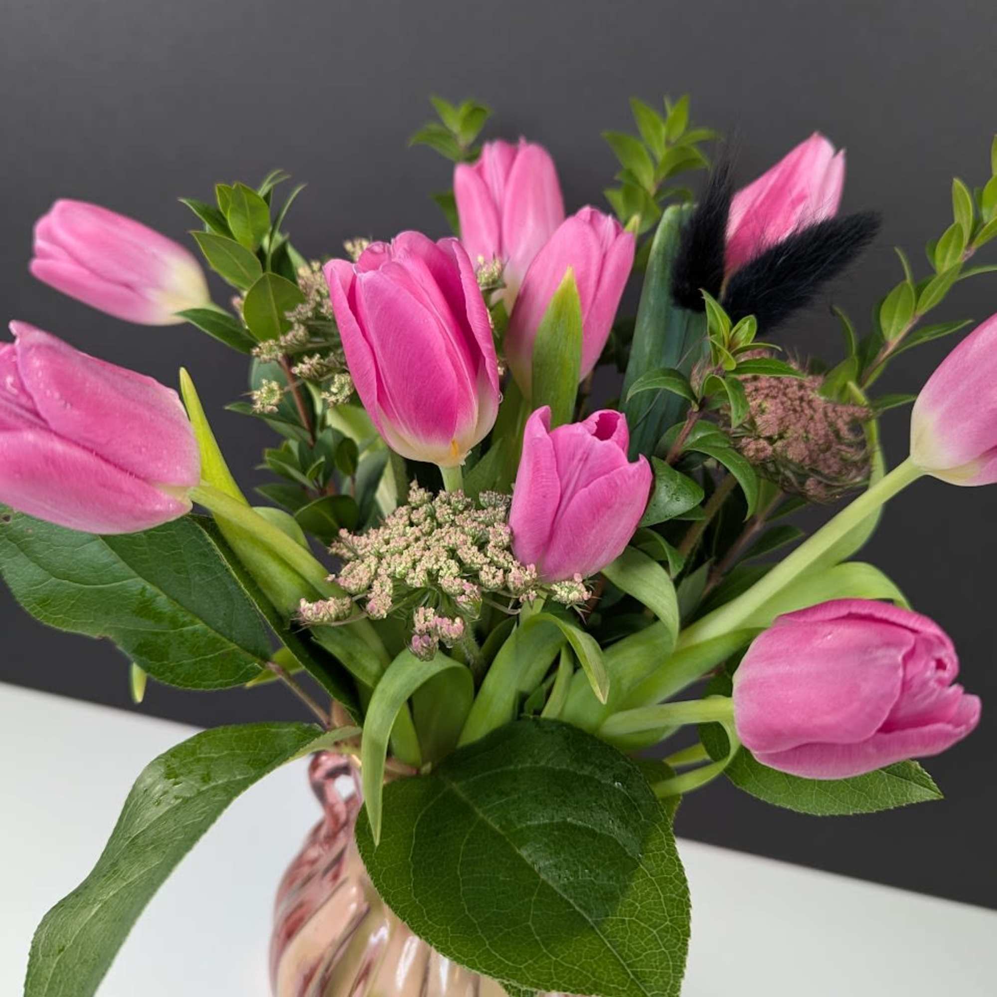 Pink tulips arranged in a pink ribbed glass vase against a dark background
