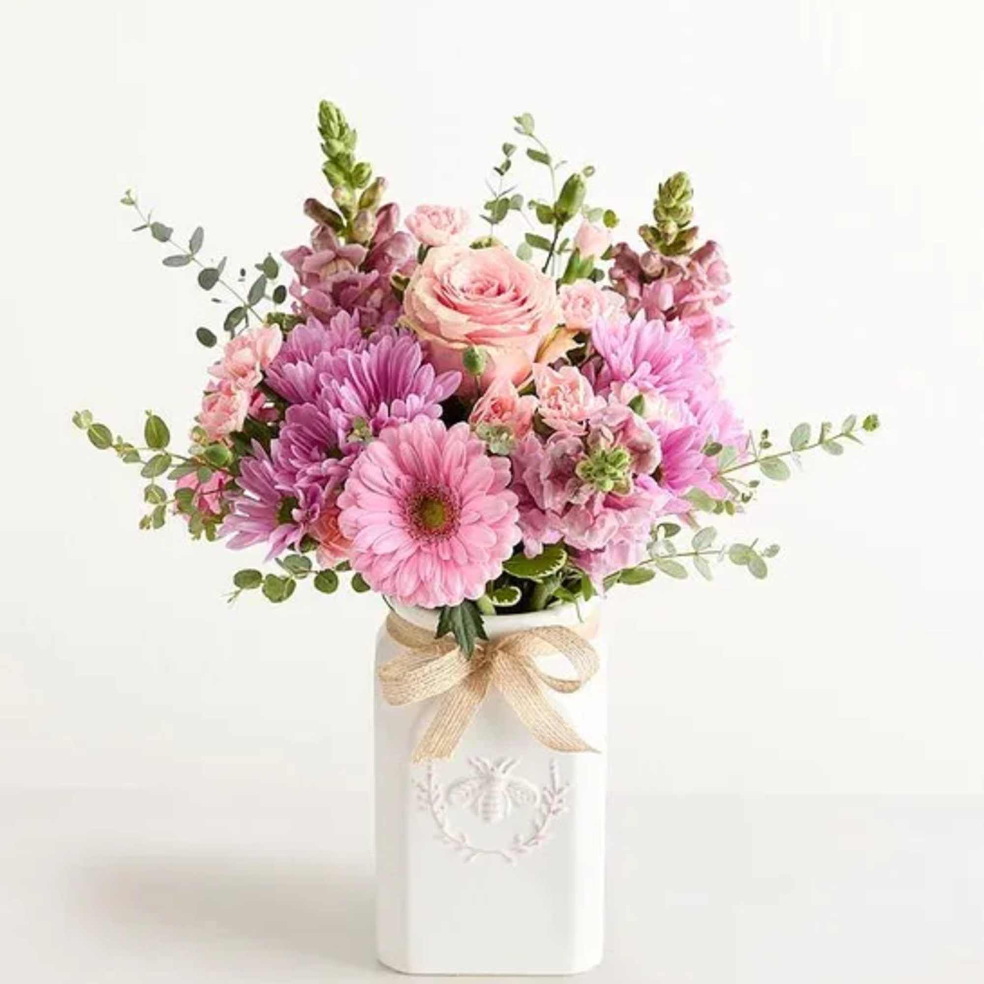 Pink and lavender flower arrangement in a white ceramic vase with a bow