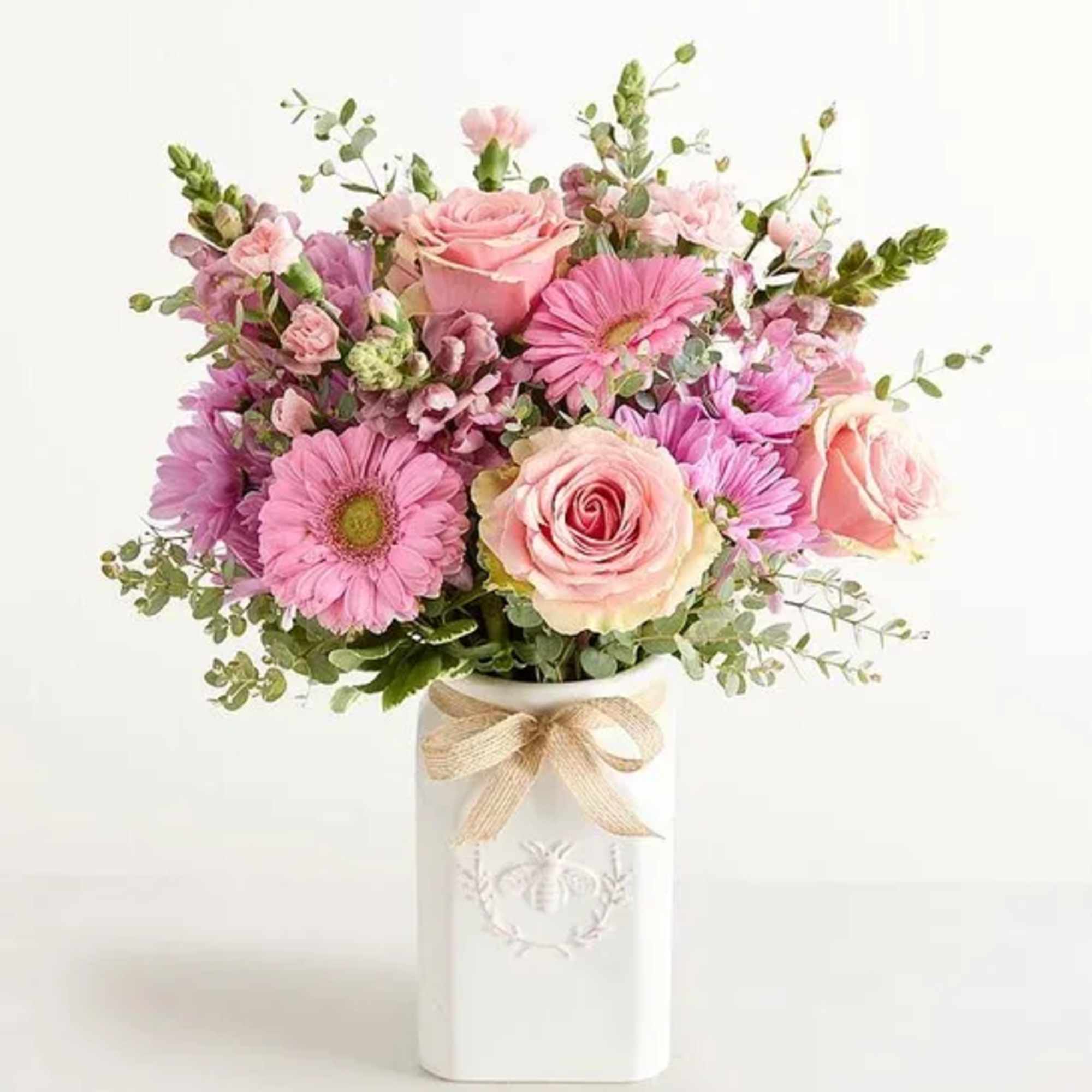 Pink roses, gerbera daisies, and mums in a tall white ceramic vase with a bow