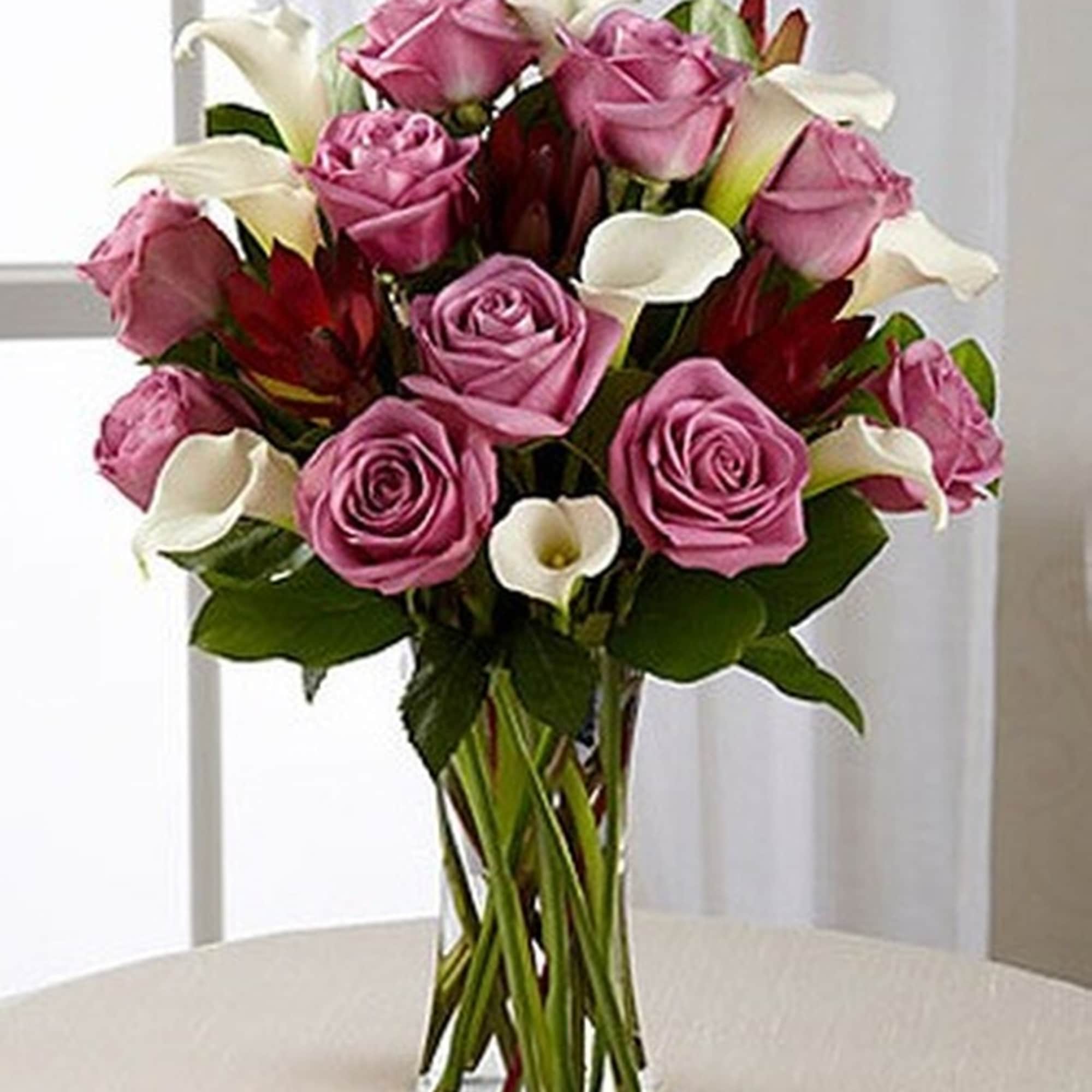 Tall glass vase of lavender roses, white calla lilies, and red accent blooms