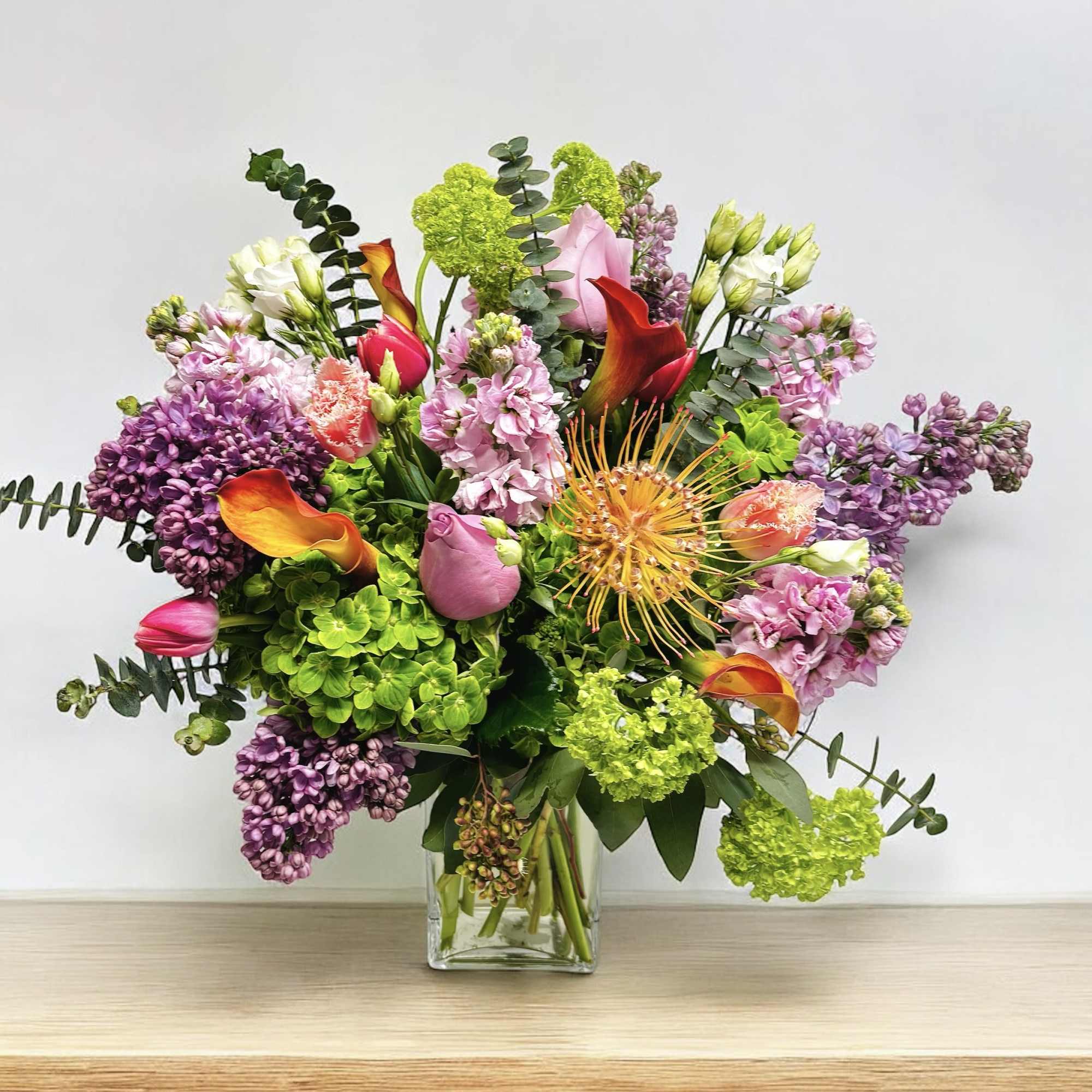 Mixed bouquet in a clear glass vase with pink, purple, green, and orange flowers