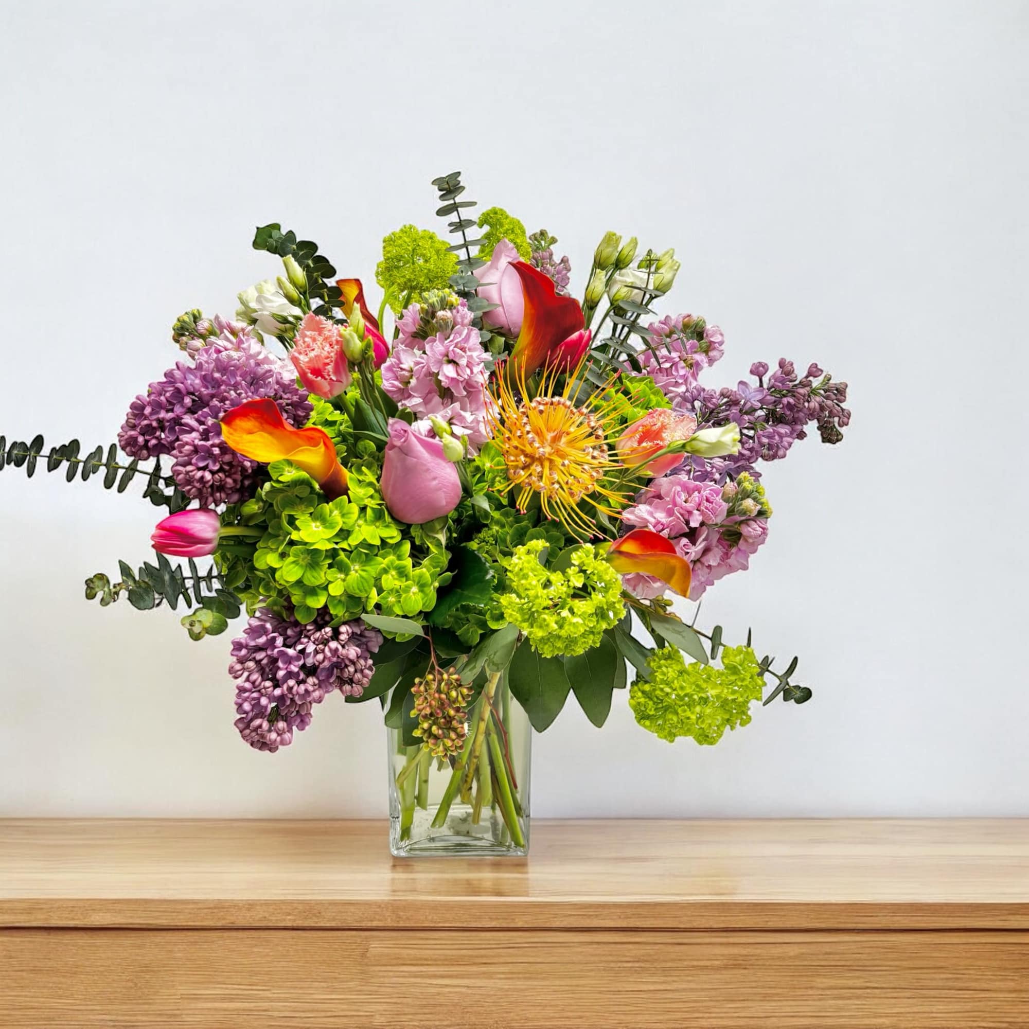 Colorful bouquet in a clear glass vase with calla lilies and purple blooms