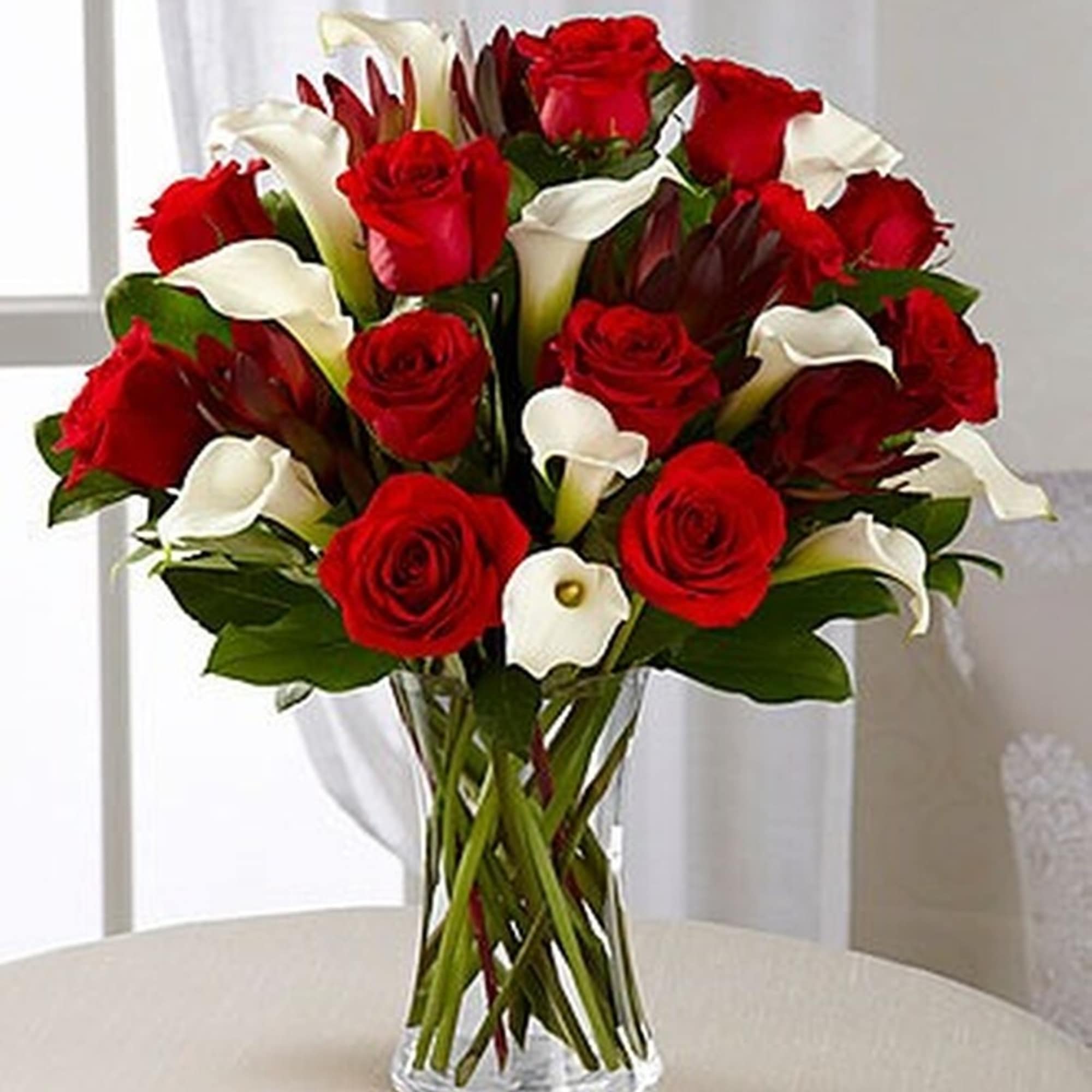 Arrangement of red roses and white calla lilies in a clear glass vase on a light table