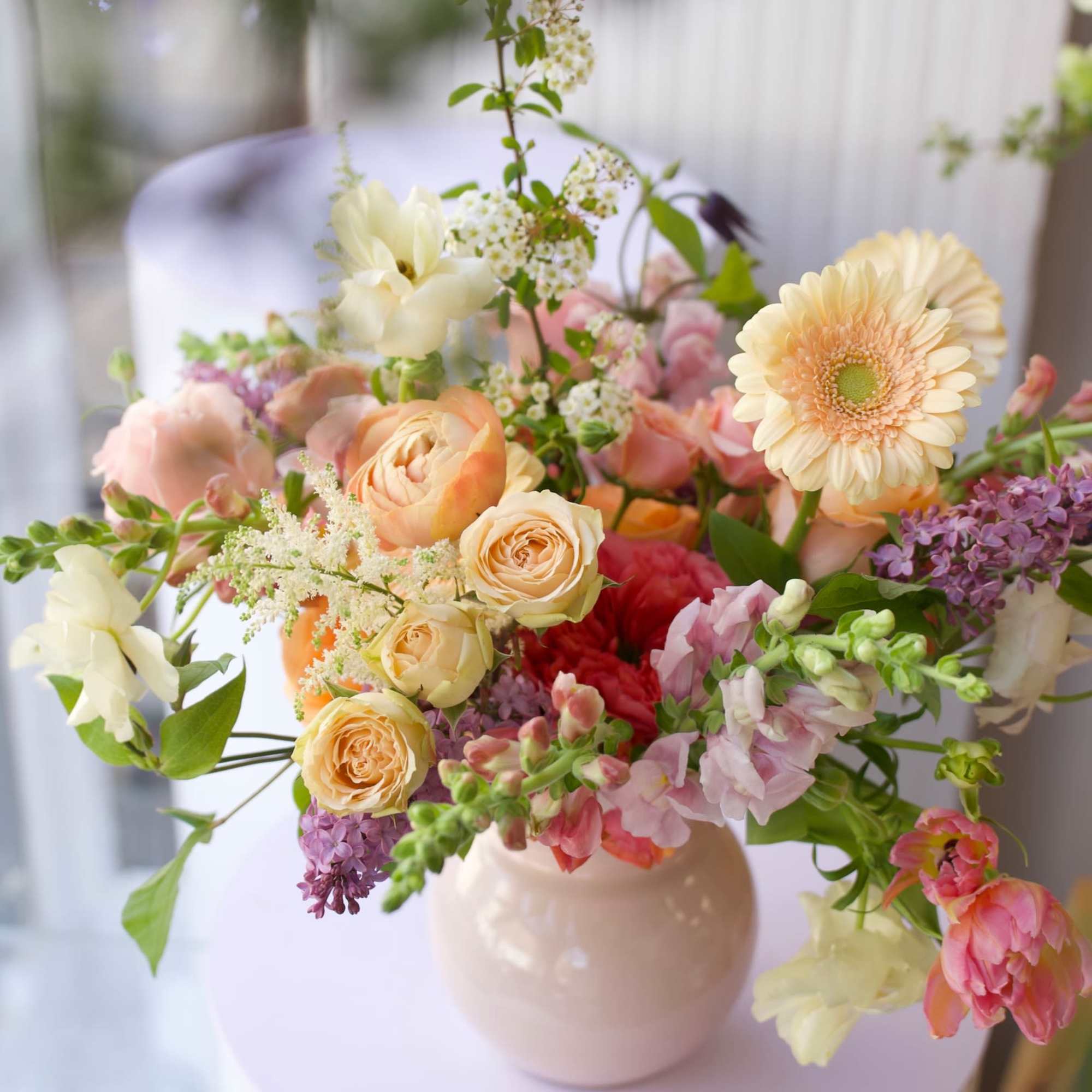 A soft, garden-style floral arrangement featuring apricot garden roses, ranunculus, tulips, snapdragons