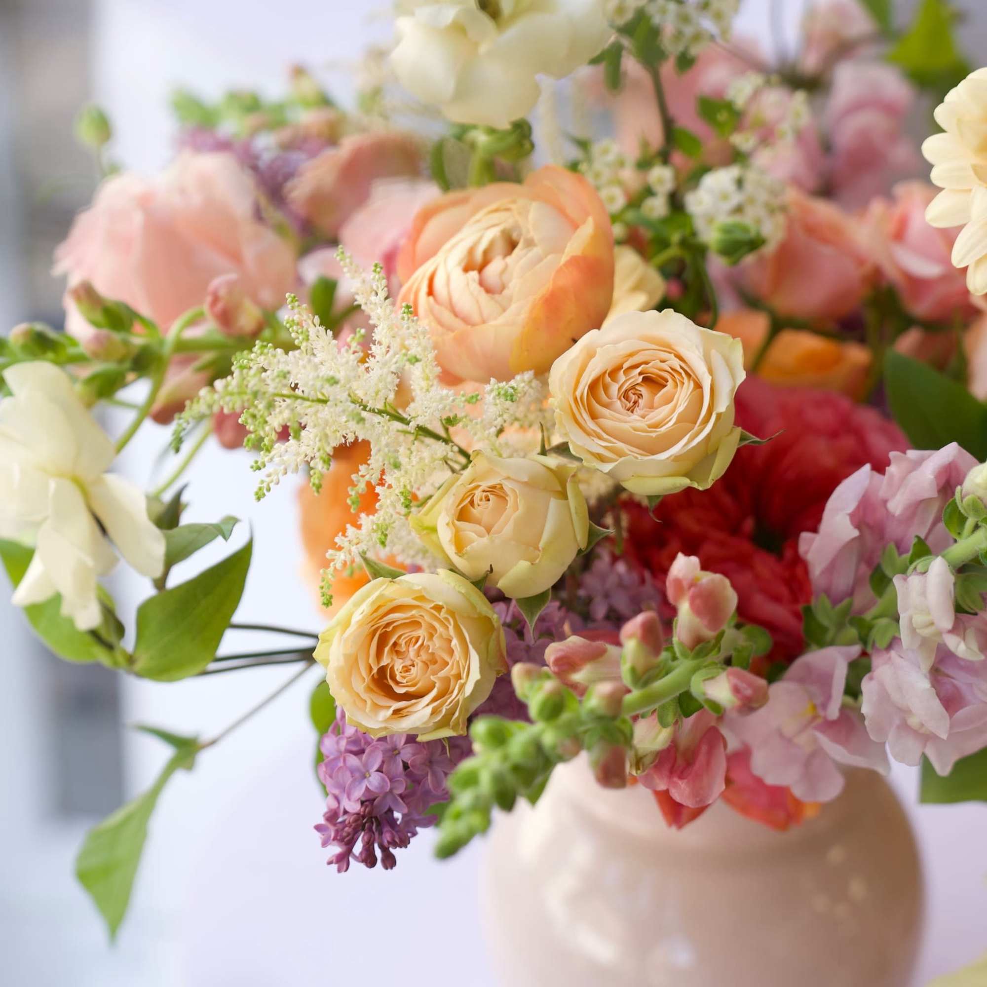 A soft, garden-style floral arrangement featuring apricot garden roses, ranunculus, tulips, snapdragons