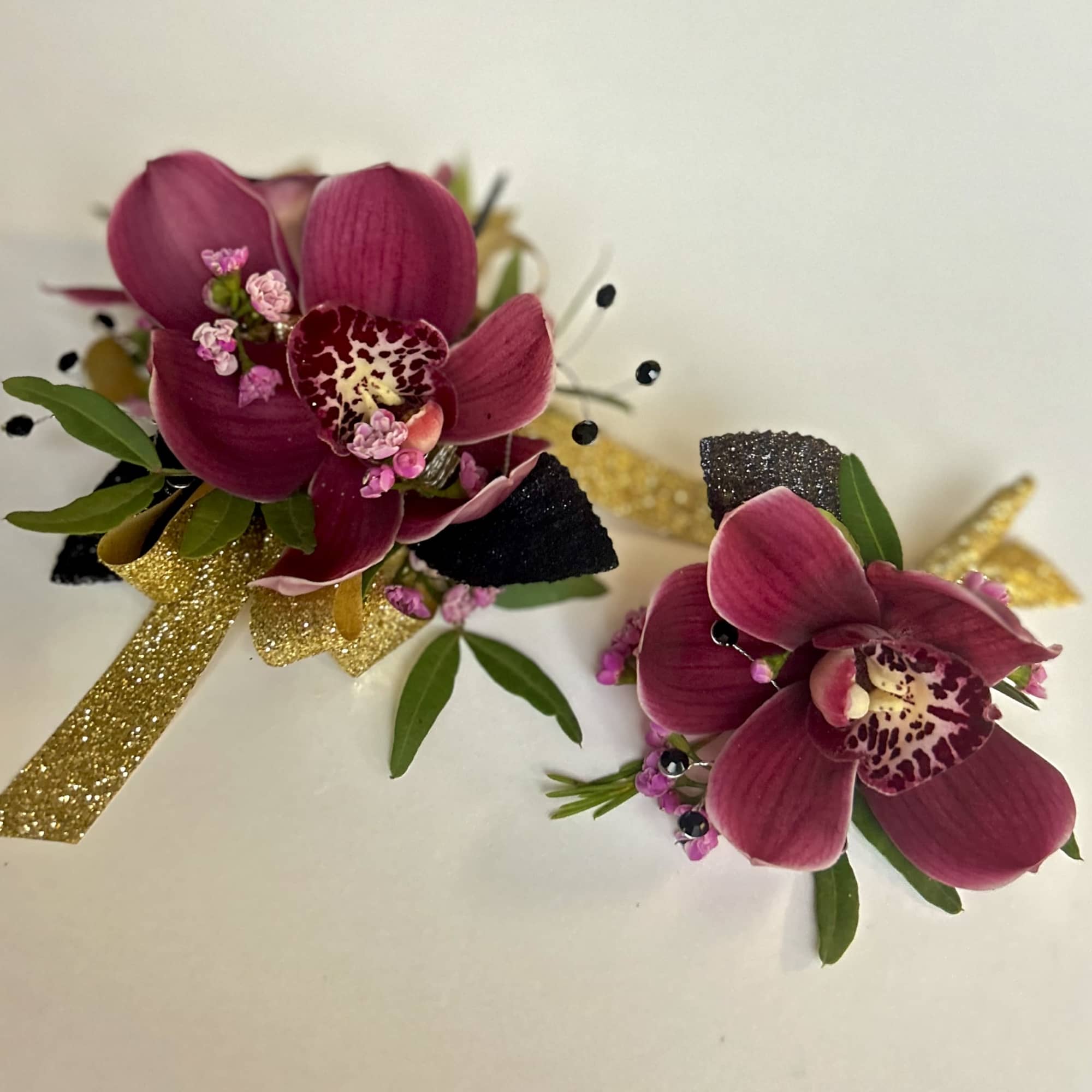 Corsage and boutonniere with burgundy cymbidium orchids, pink accents, and gold glitter ribbon.