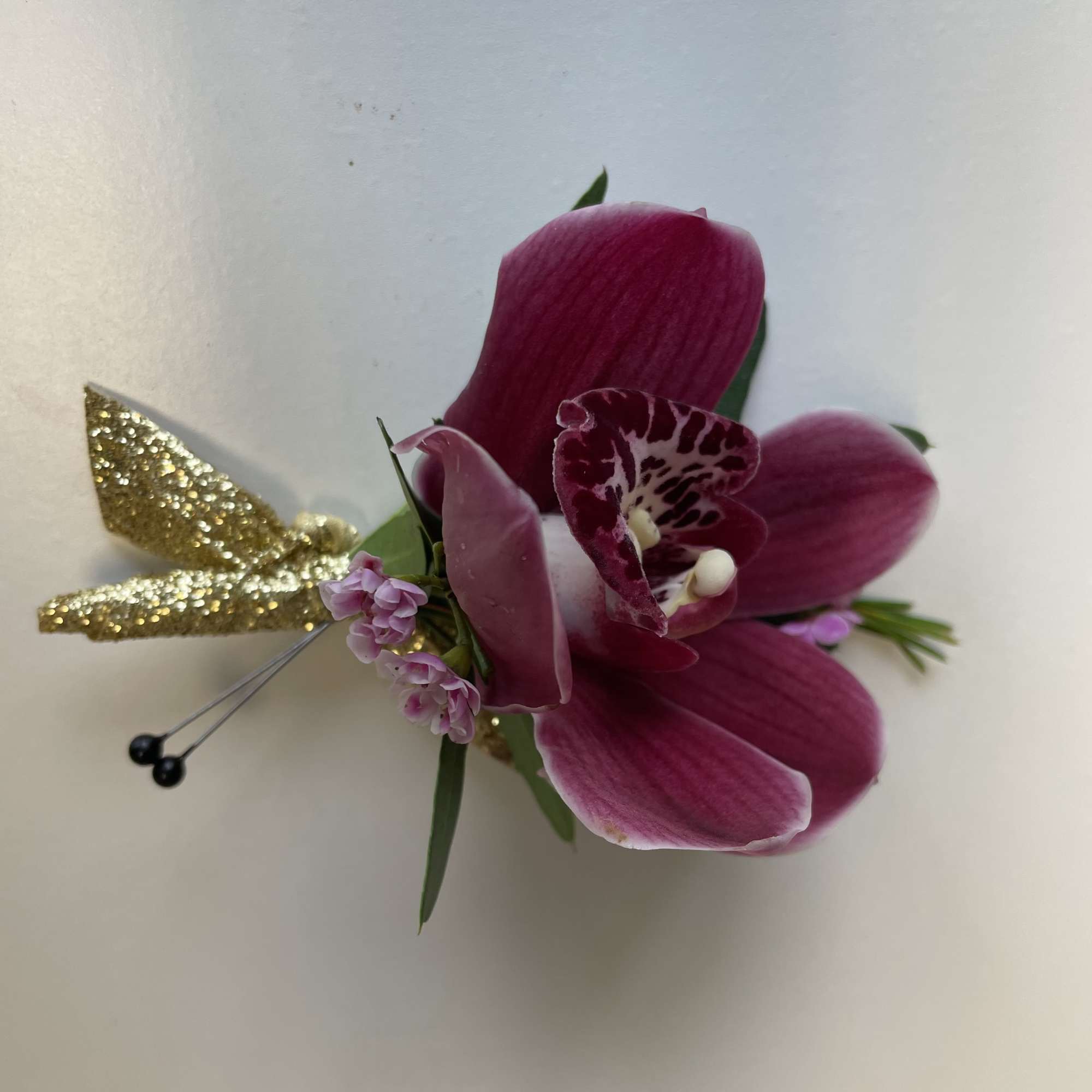 Magenta orchid corsage with small pink blooms and gold glitter accents on a white background
