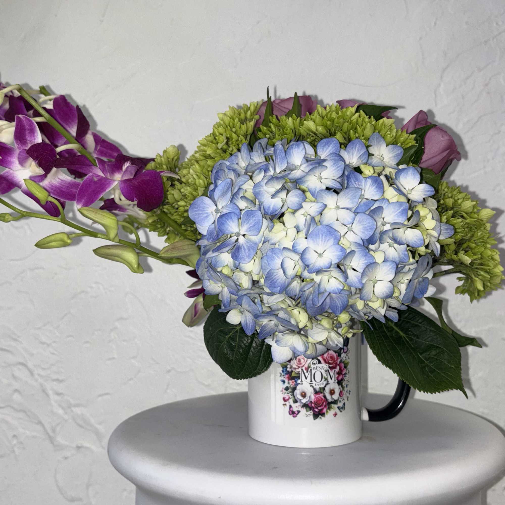 Blue and green hydrangea come together, with lavender roses and orchids in