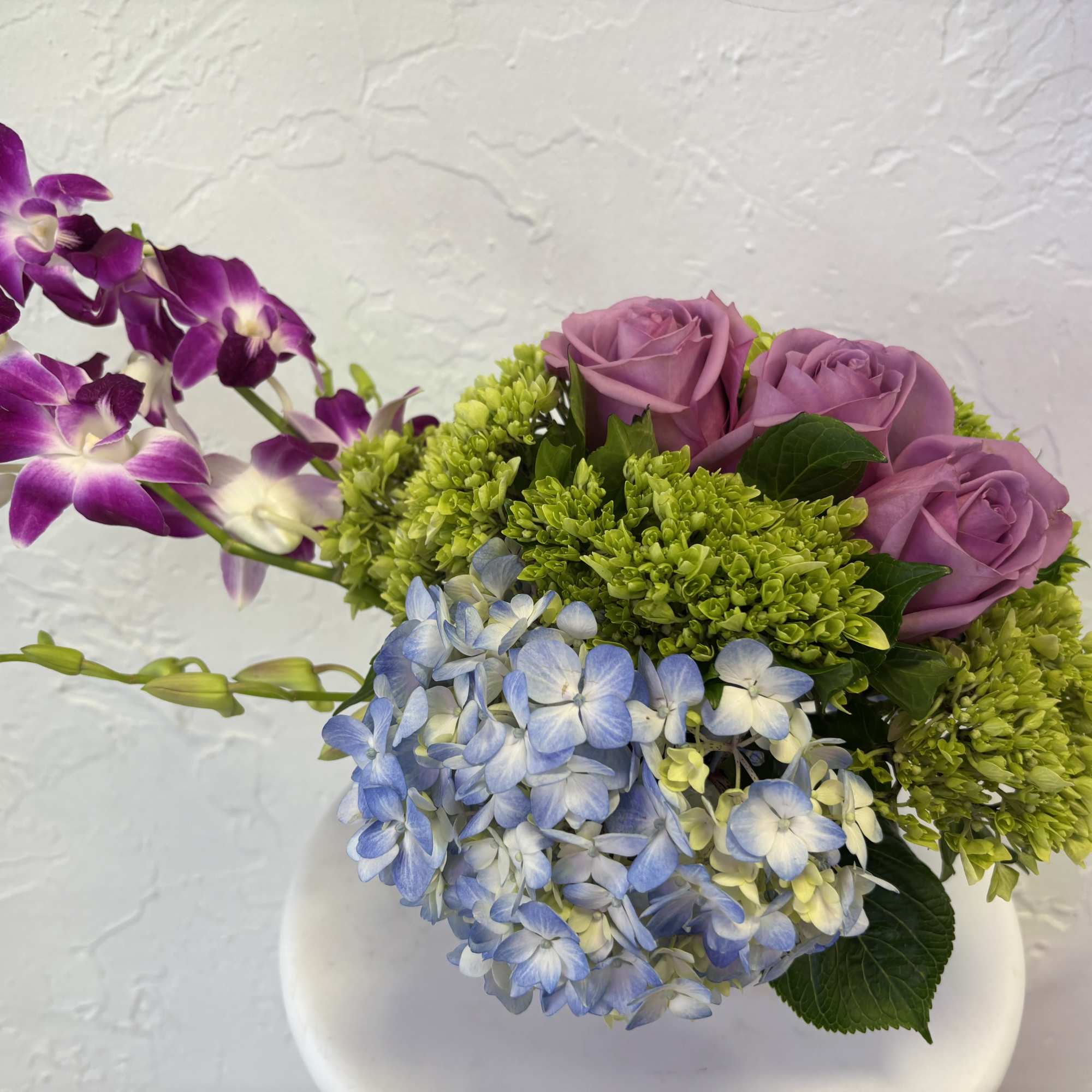Blue and green hydrangea come together, with lavender roses and orchids in