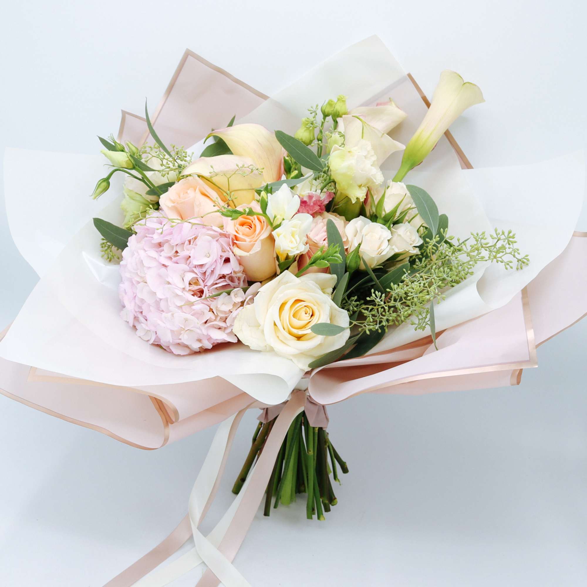 Hand-tied bouquet of cream roses, pink hydrangea, and pale calla lilies wrapped in blush paper.