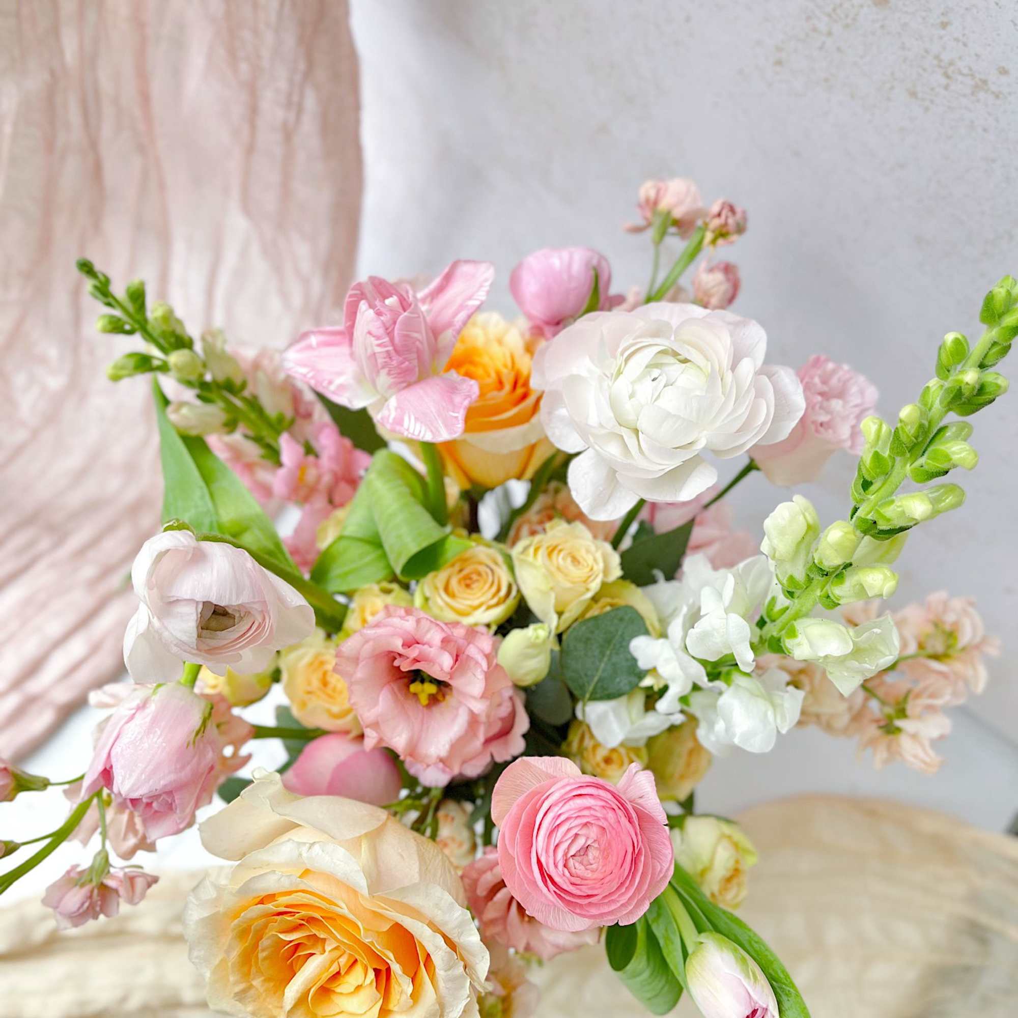 A soft and radiant spring vase arrangement featuring roses, ranunculus, tulips, lisianthus