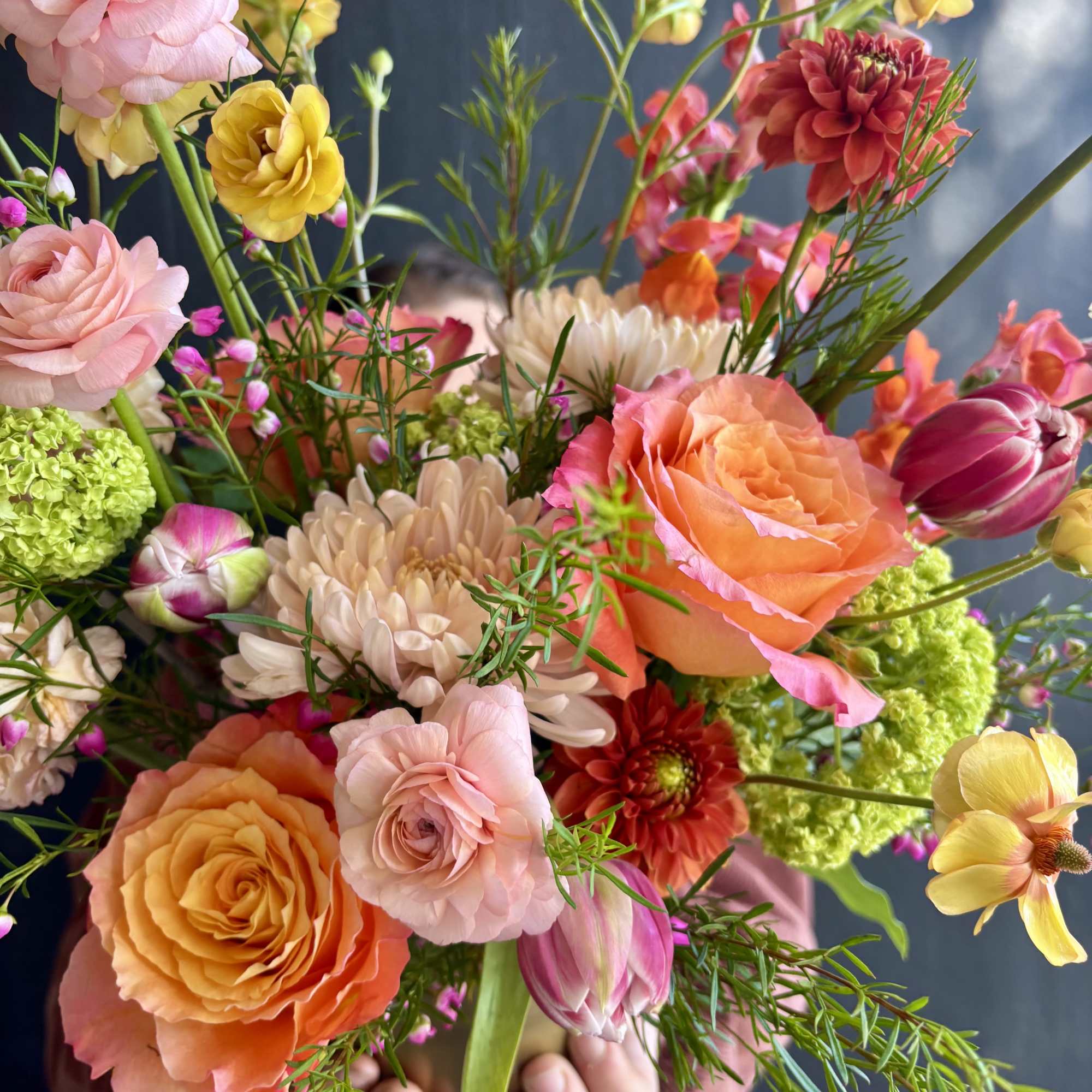 Hand-tied bouquet of peach and pink roses, ranunculus, tulips, and mixed flowers held in both hands