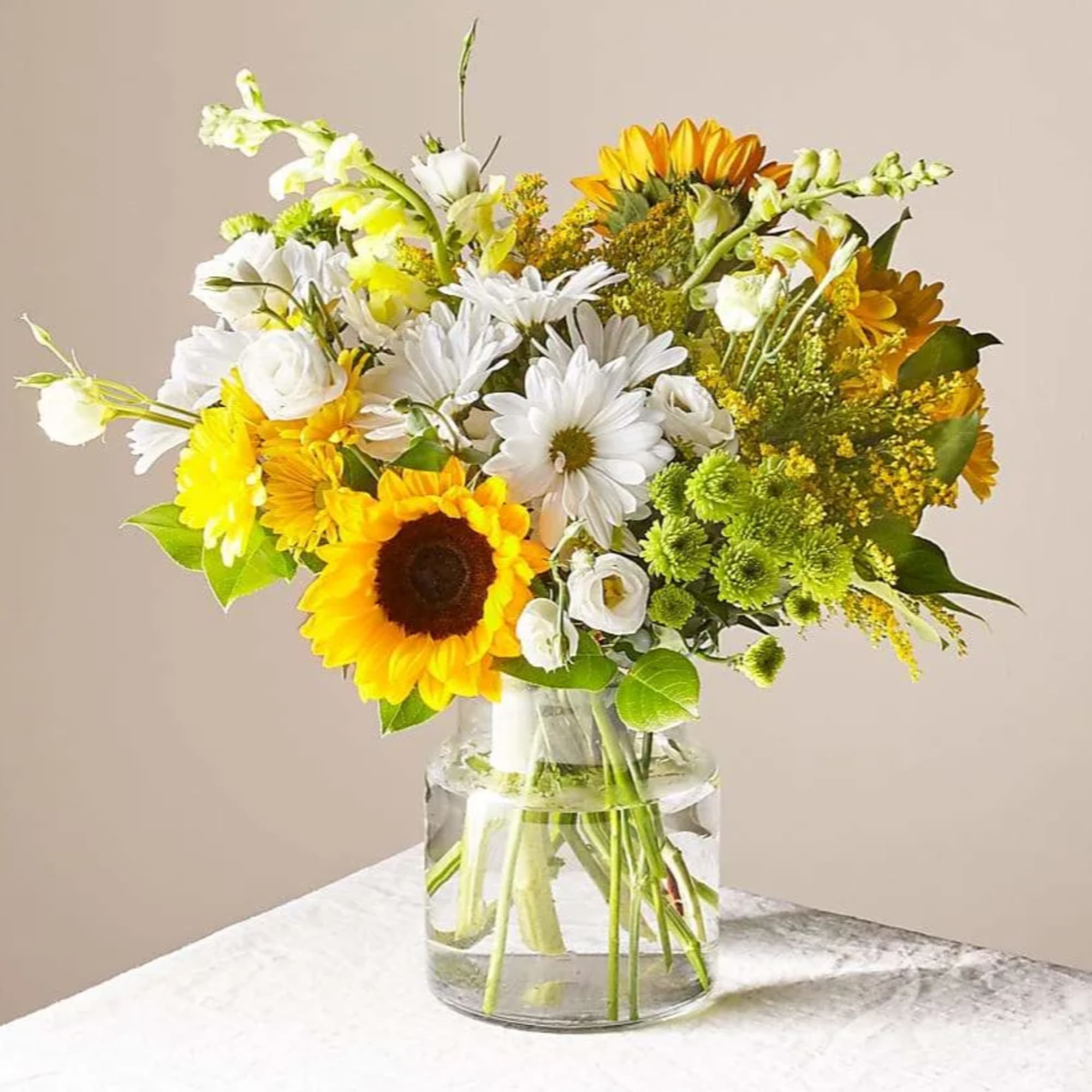 Yellow sunflowers, white daisies, and green accents arranged in a clear glass vase.