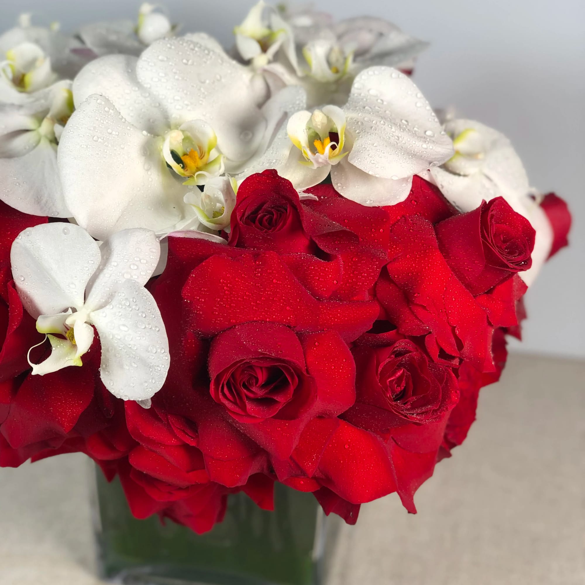 Low cube arrangement of red roses topped with white orchids in a clear glass vase