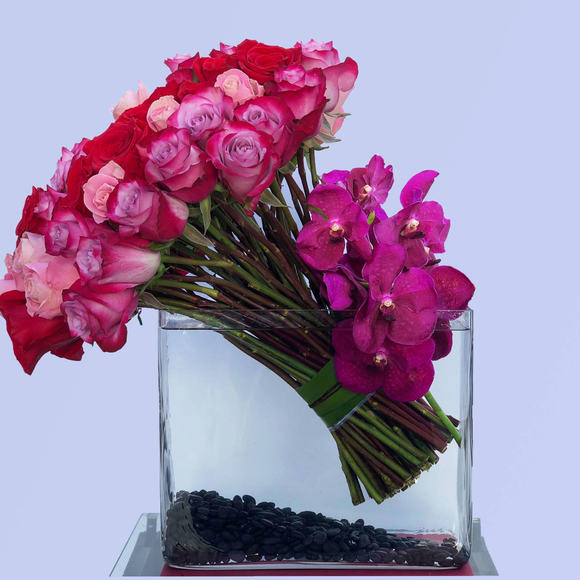 Pink and red roses with magenta orchids in a clear glass vase