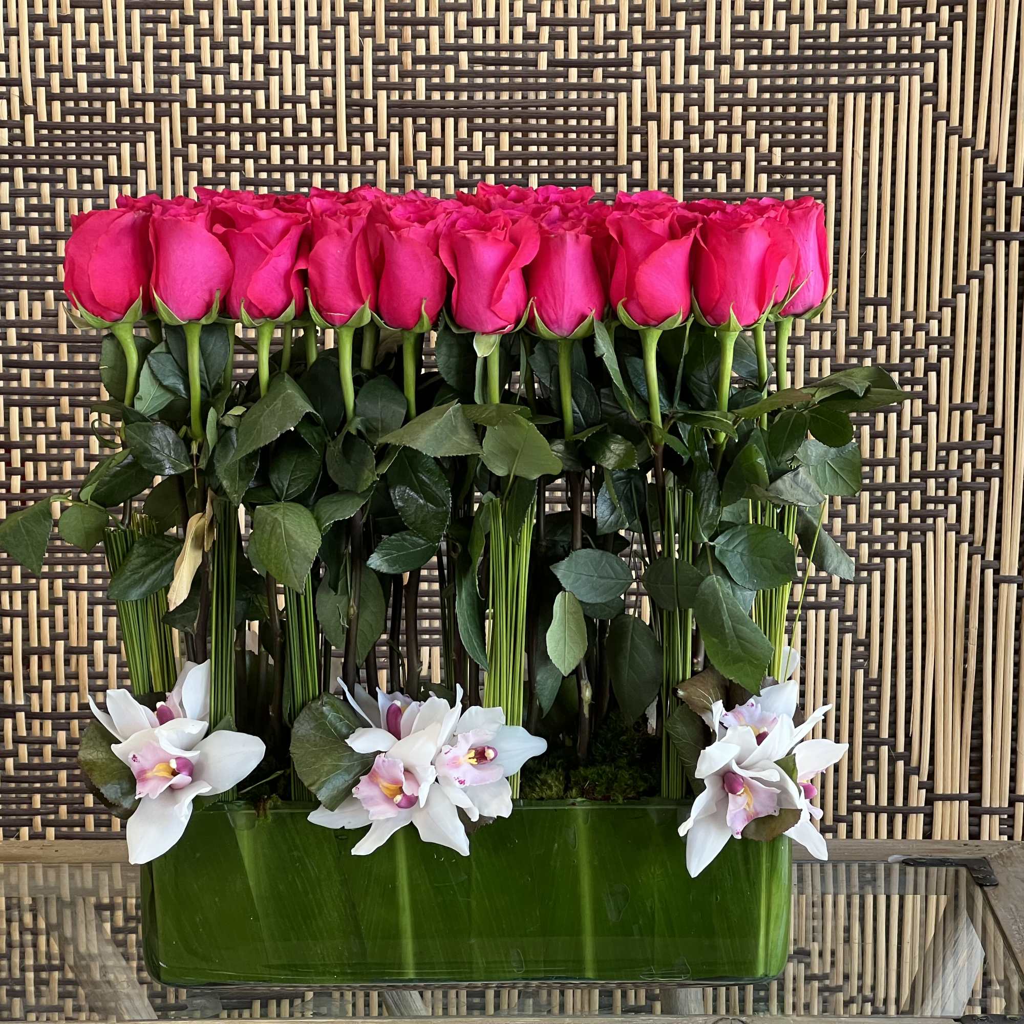 A modern arrangement of Roses and Cymbidium Orchids, presented in a leaf-lined