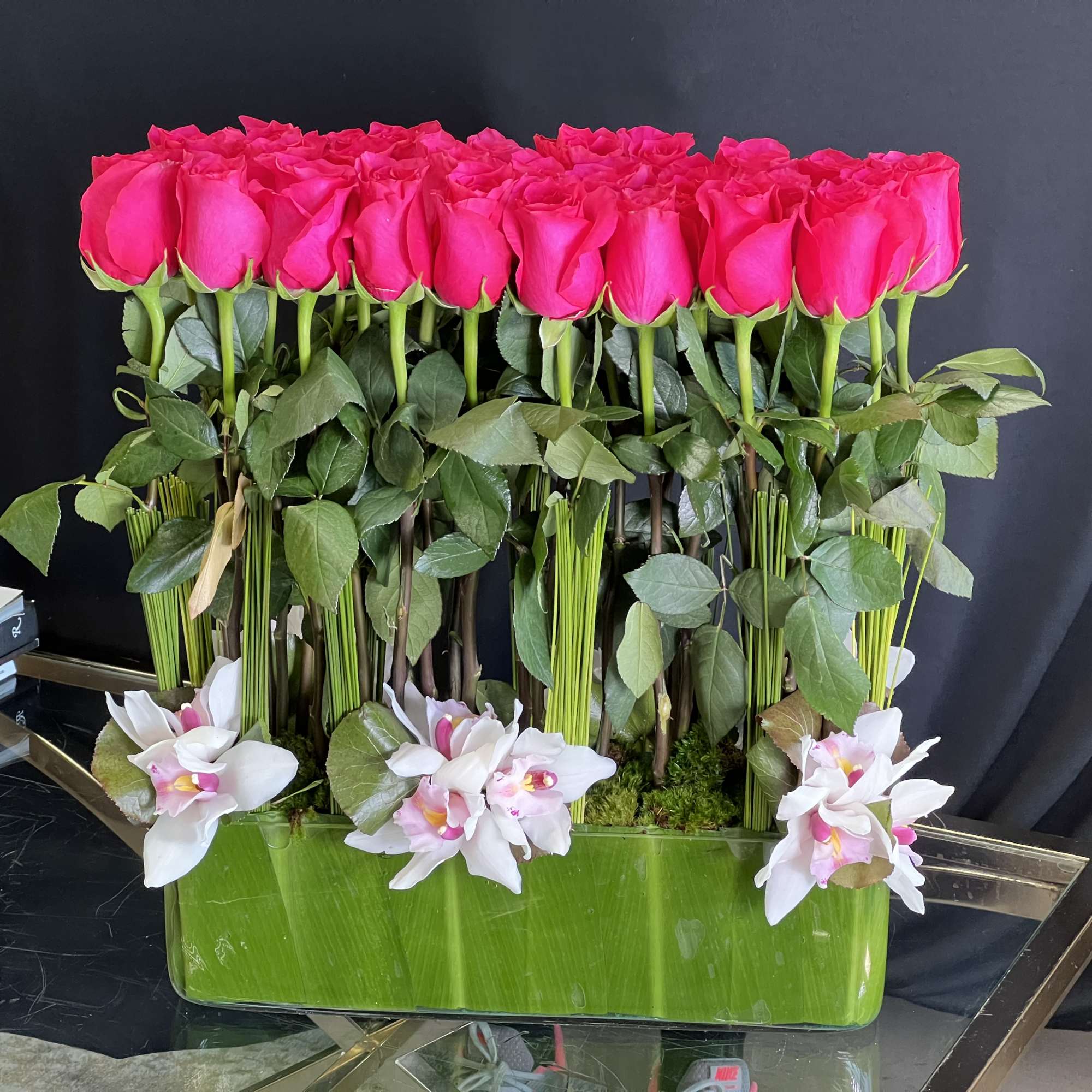 A modern arrangement of Roses and Cymbidium Orchids, presented in a leaf-lined