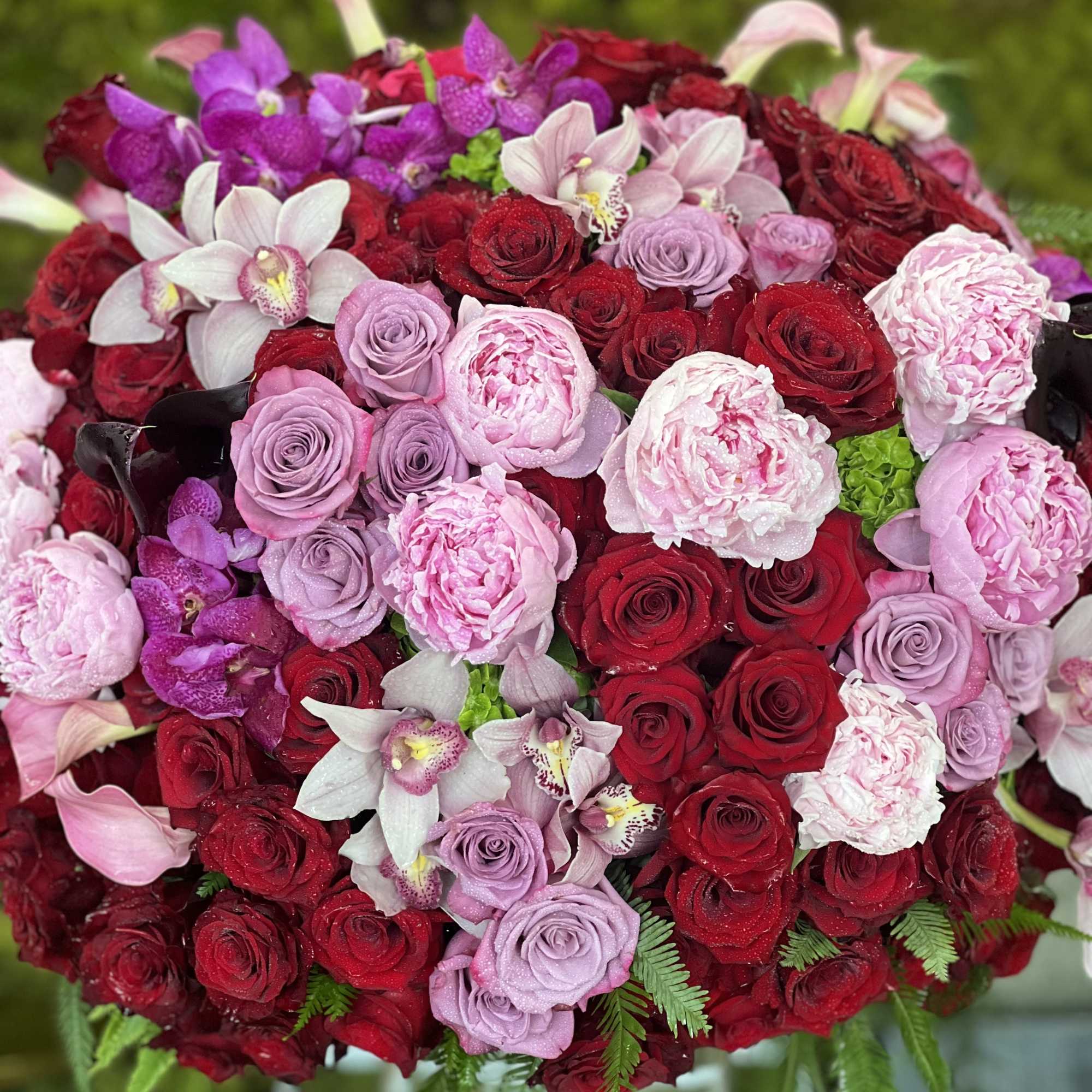 Large bouquet of red, pink, and lavender roses with orchids