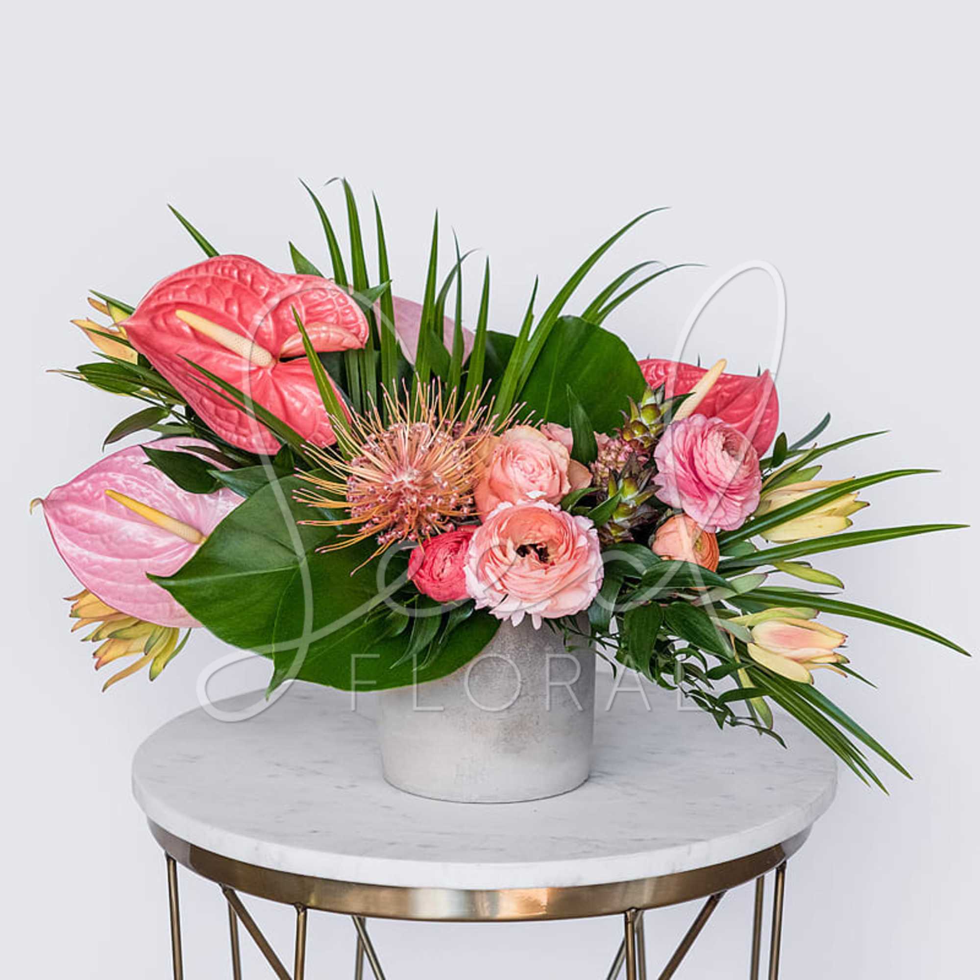 Pink tropical flower arrangement with ranunculus in a white ceramic vase on a marble table