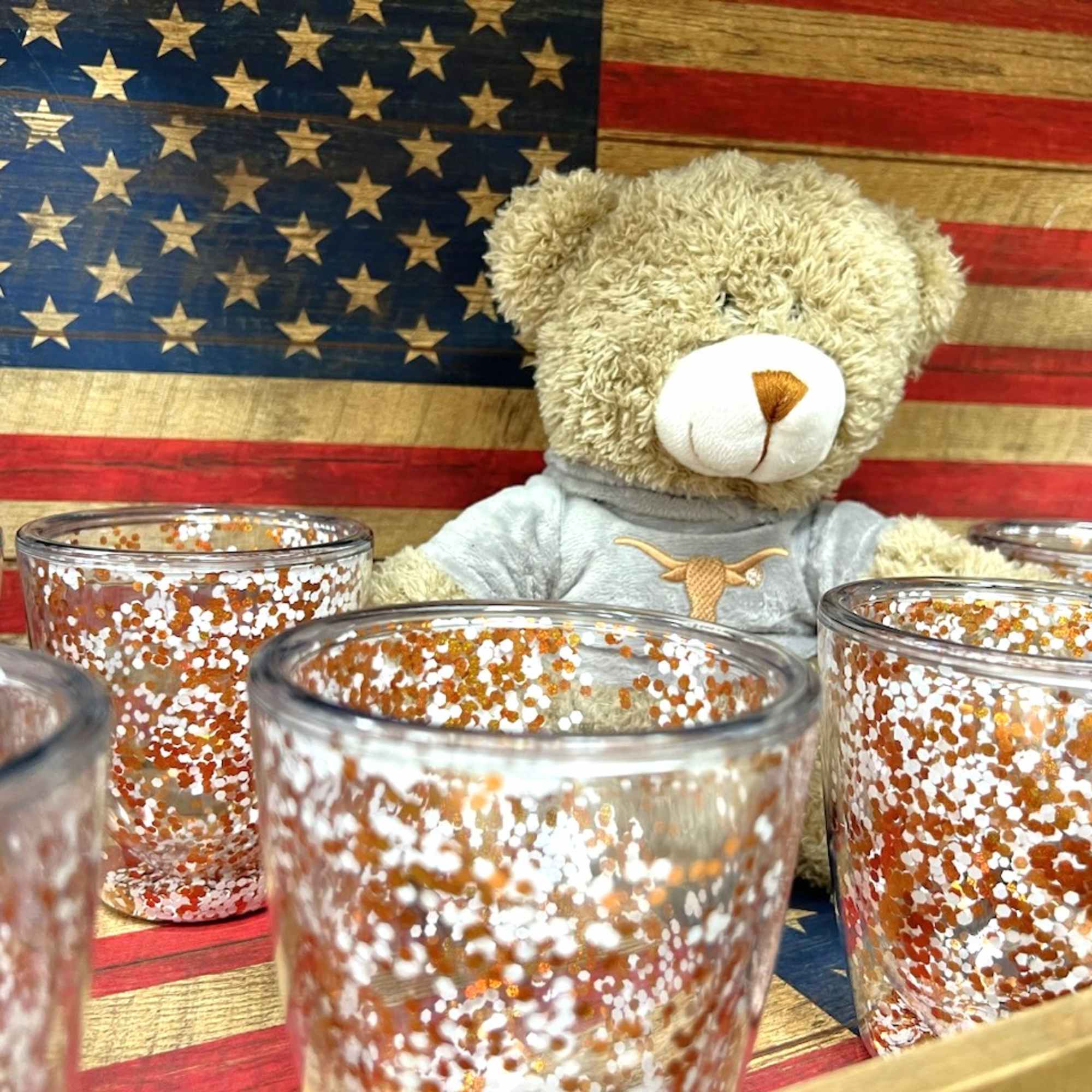Teddy bear behind glittered glass votive holders in front of an American flag backdrop