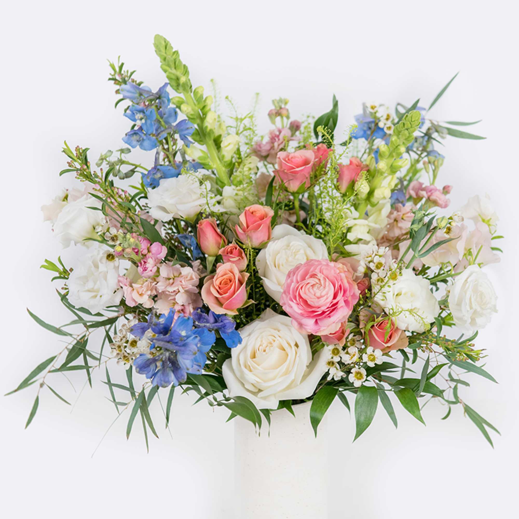 Mixed bouquet of roses, ranunculus, and blue flowers in a white vase