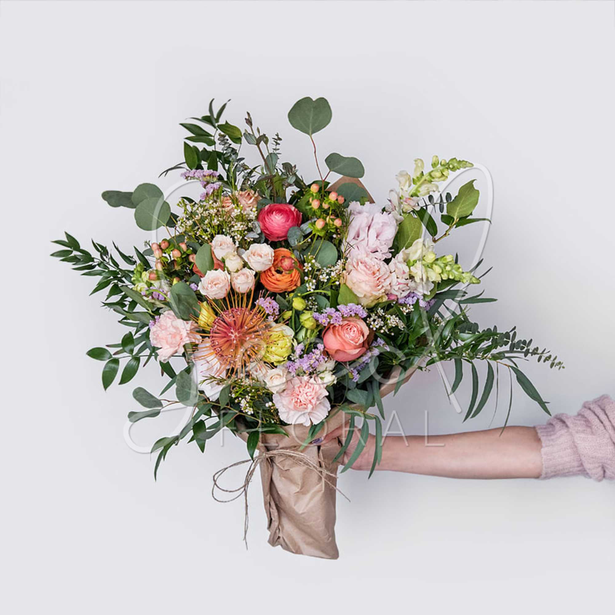 Handheld bouquet of mixed pink and peach flowers with greenery