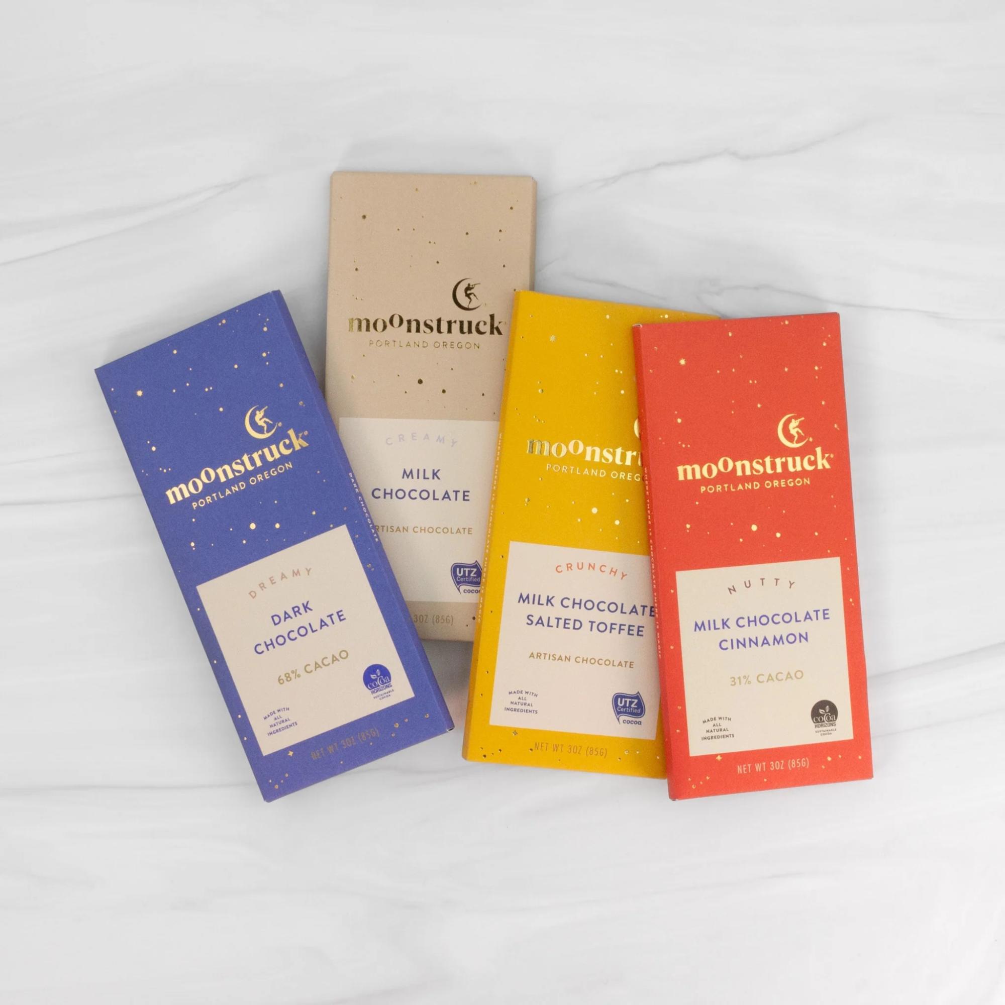 Four boxed chocolate bars in blue, beige, yellow, and red packaging