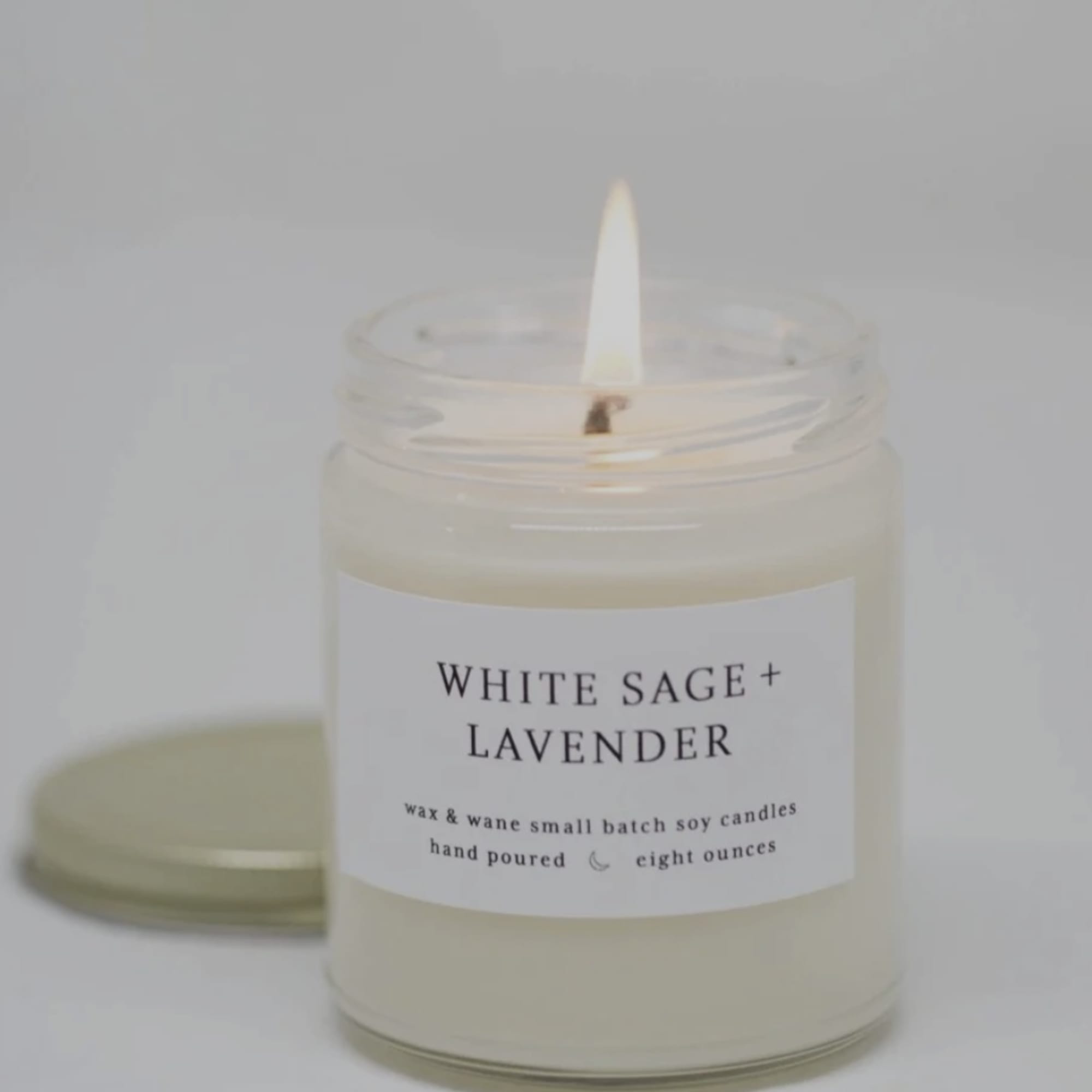 Lit white candle in a glass jar labeled White Sage + Lavender