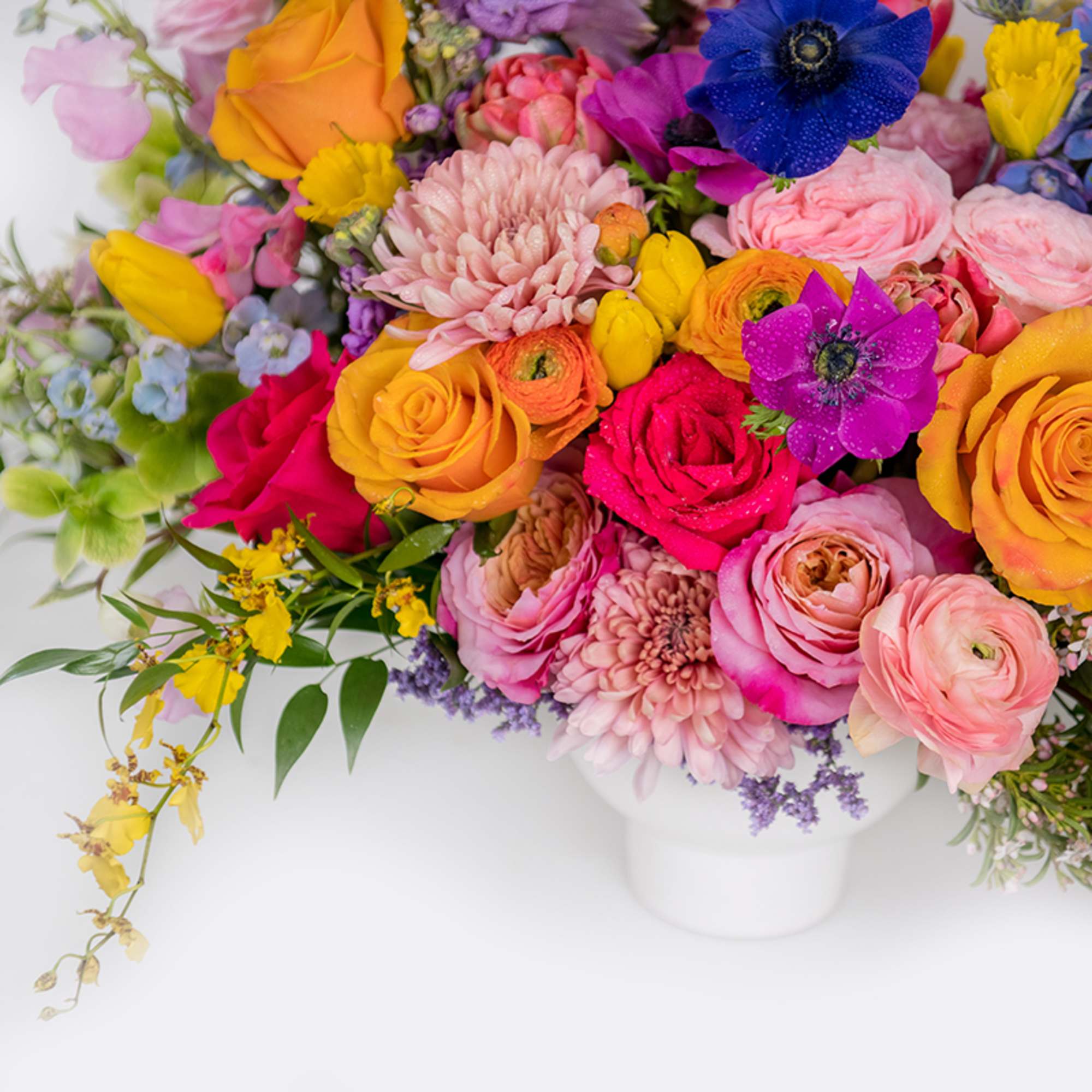 Bright mixed bouquet of roses, ranunculus, anemones and other flowers in a white vase