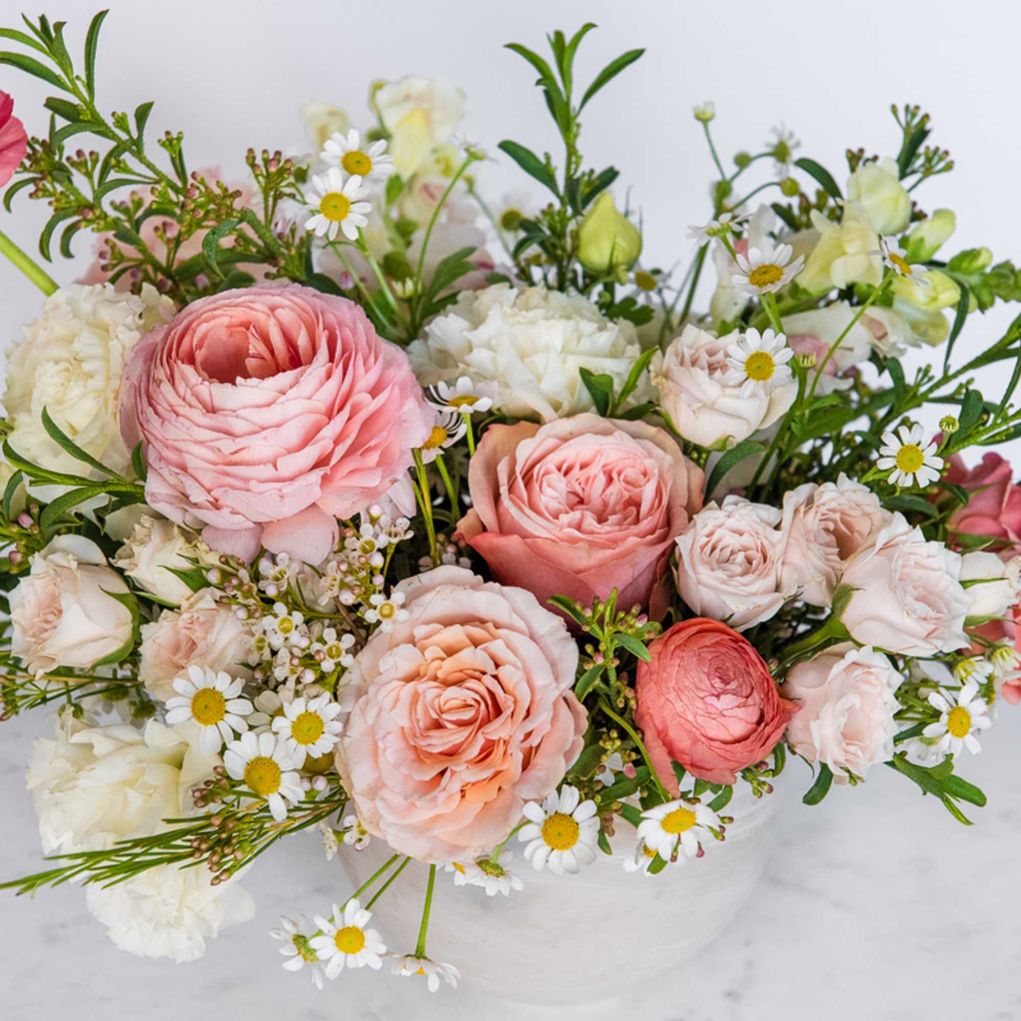 Pink and white roses with small daisy-like flowers in a white vase