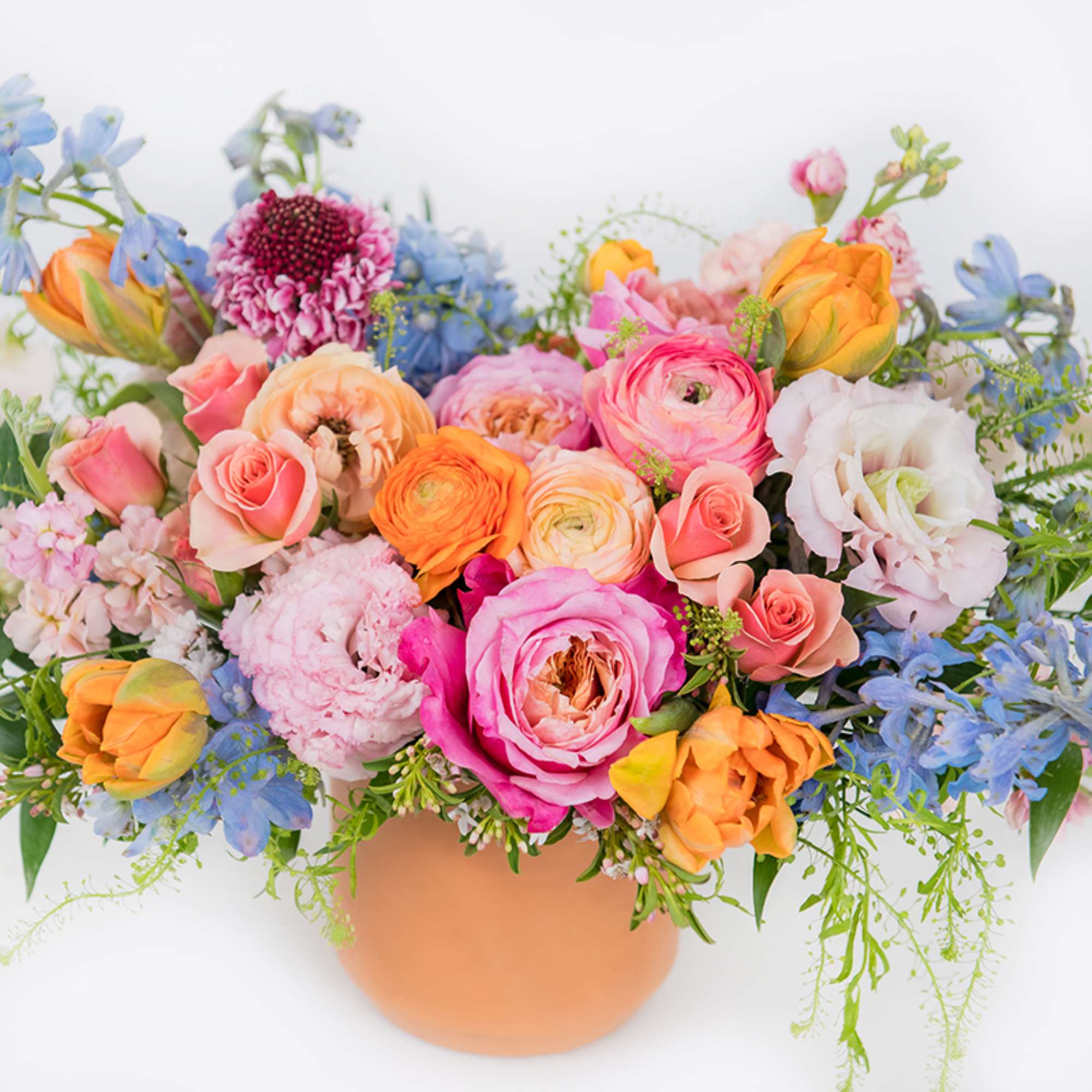 Colorful mixed bouquet in a peach vase with pink, orange, and blue flowers