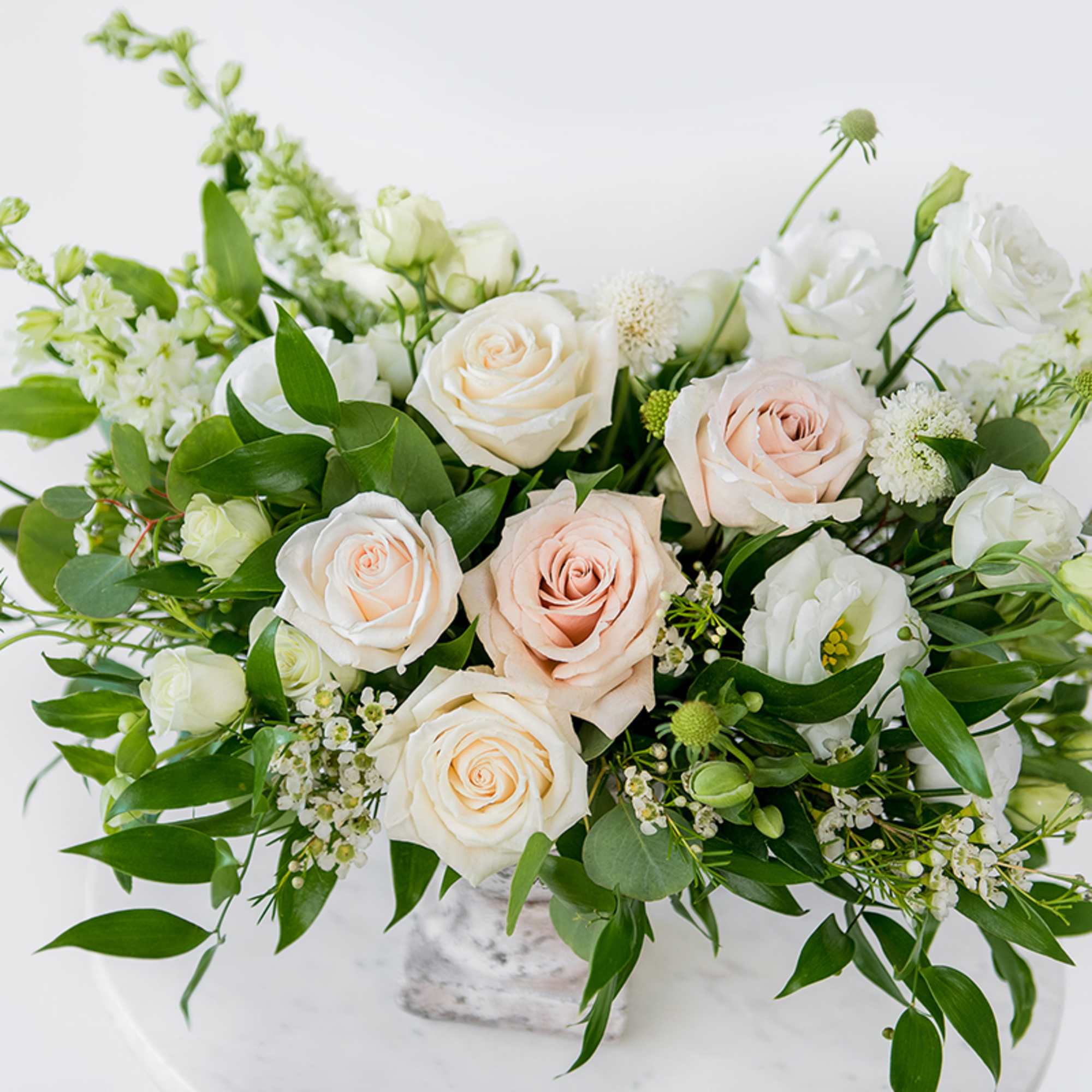 White and blush roses arranged in a low vase with greenery.