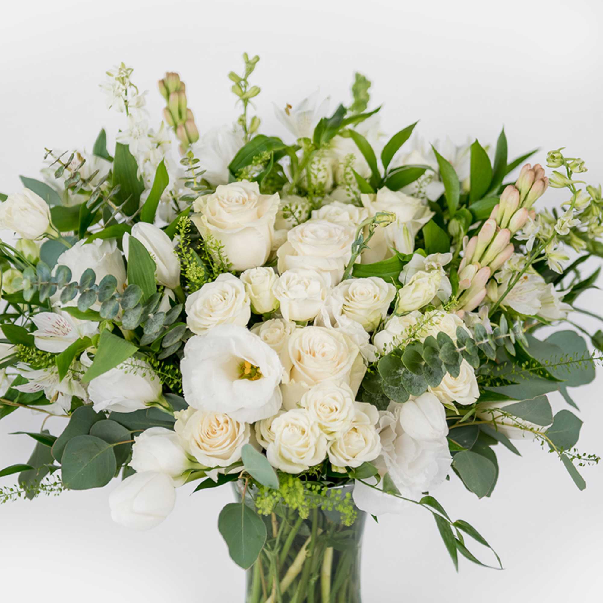 White roses and lilies arranged in a clear glass vase with greenery.