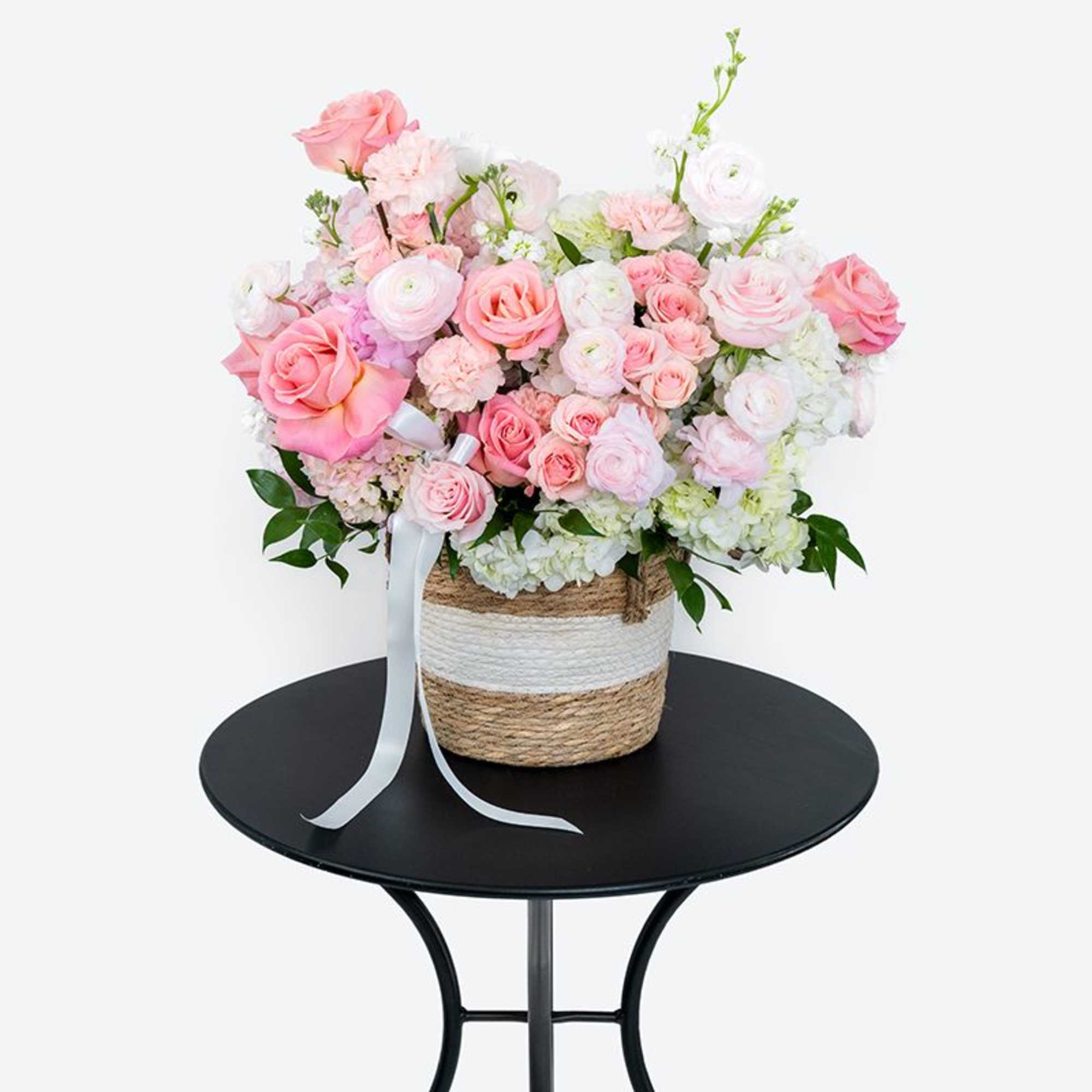 Pink and white flower arrangement in a woven basket with a ribbon