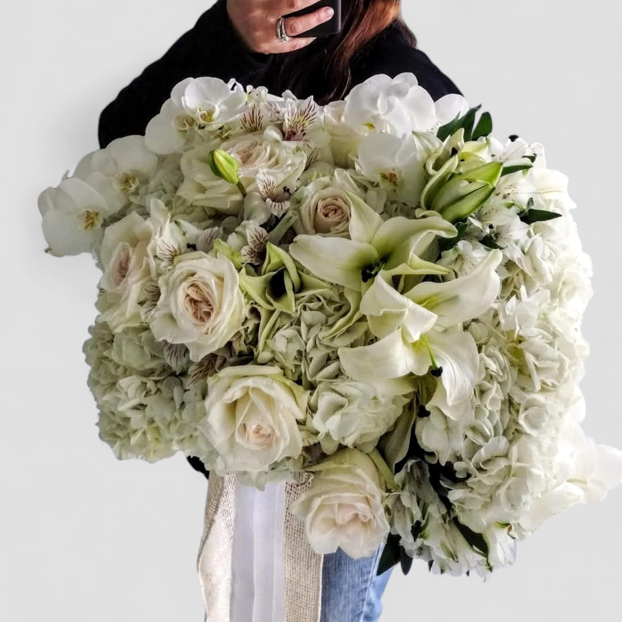 Large all-white hand-tied bouquet of roses, lilies, hydrangeas, and orchids with trailing ribbon
