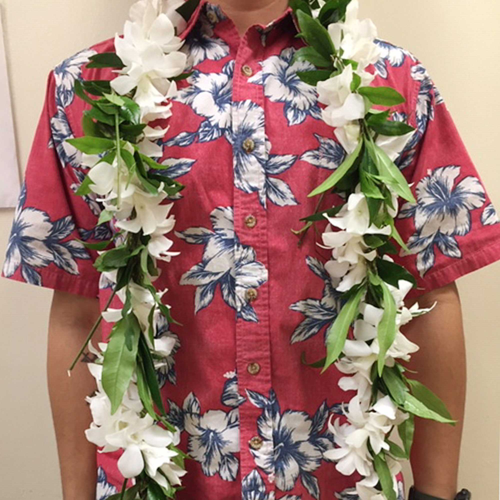 White floral leis with green accents draped around a neck over a red floral shirt