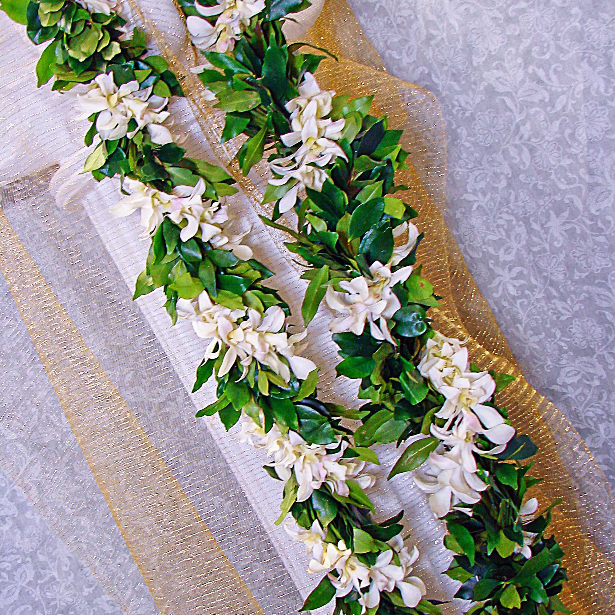 Two long garlands of white flowers with glossy green foliage on gold and white fabric