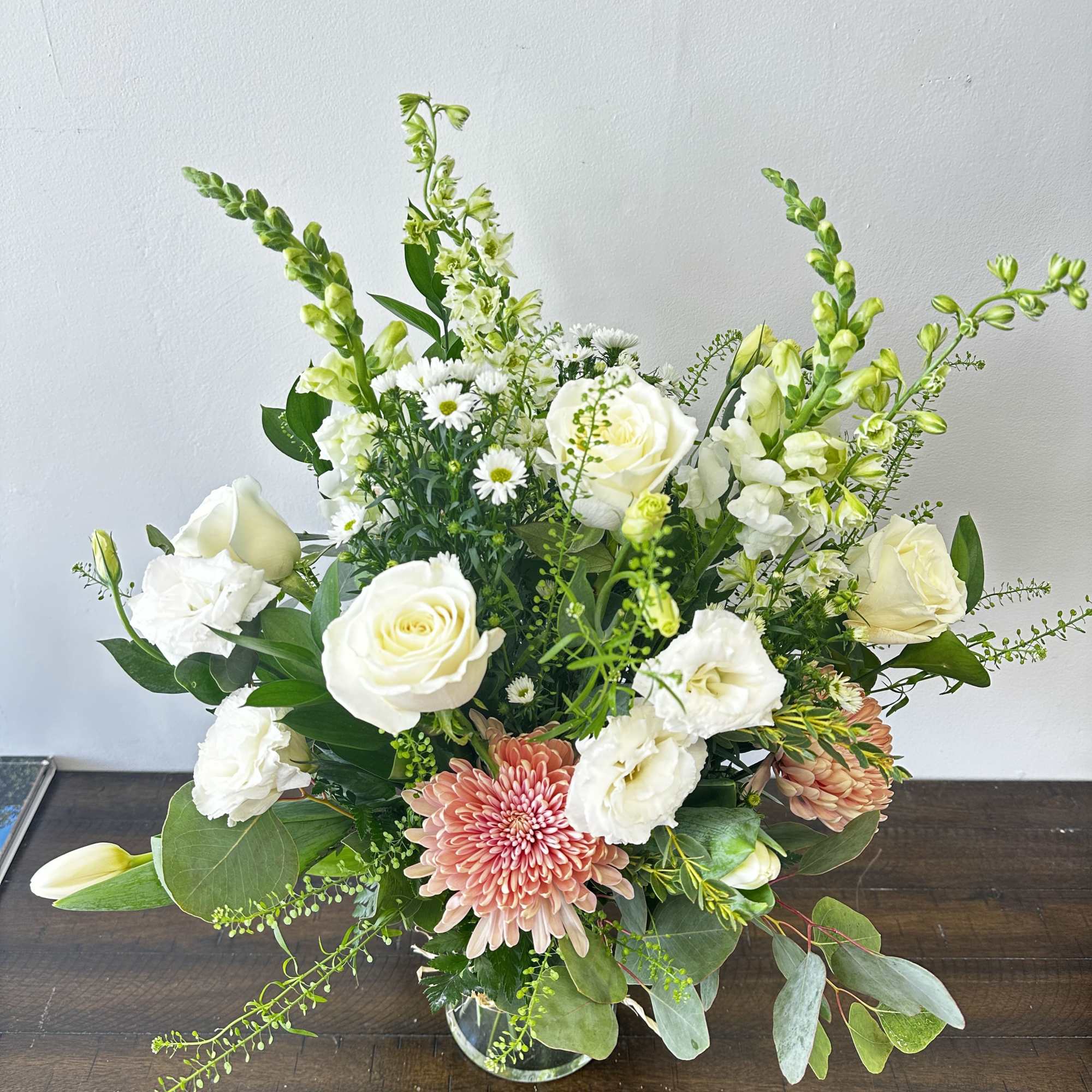 Arrangement of white roses, lisianthus, and peach chrysanthemums in a clear glass vase