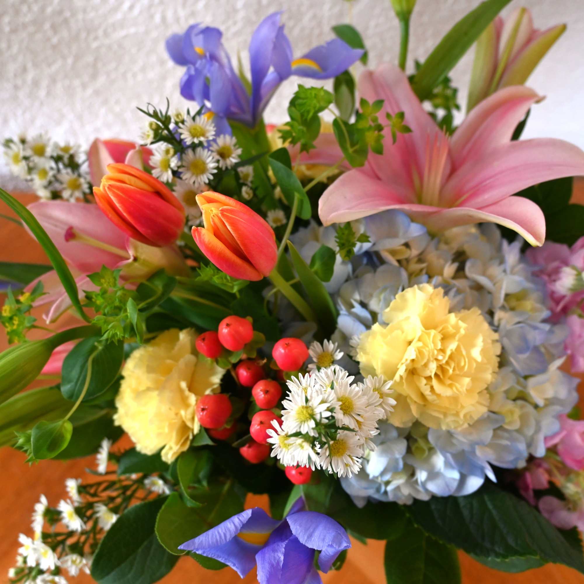 Colorful mixed bouquet with pink lilies, orange tulips, blue hydrangeas, yellow carnations, and purple irises