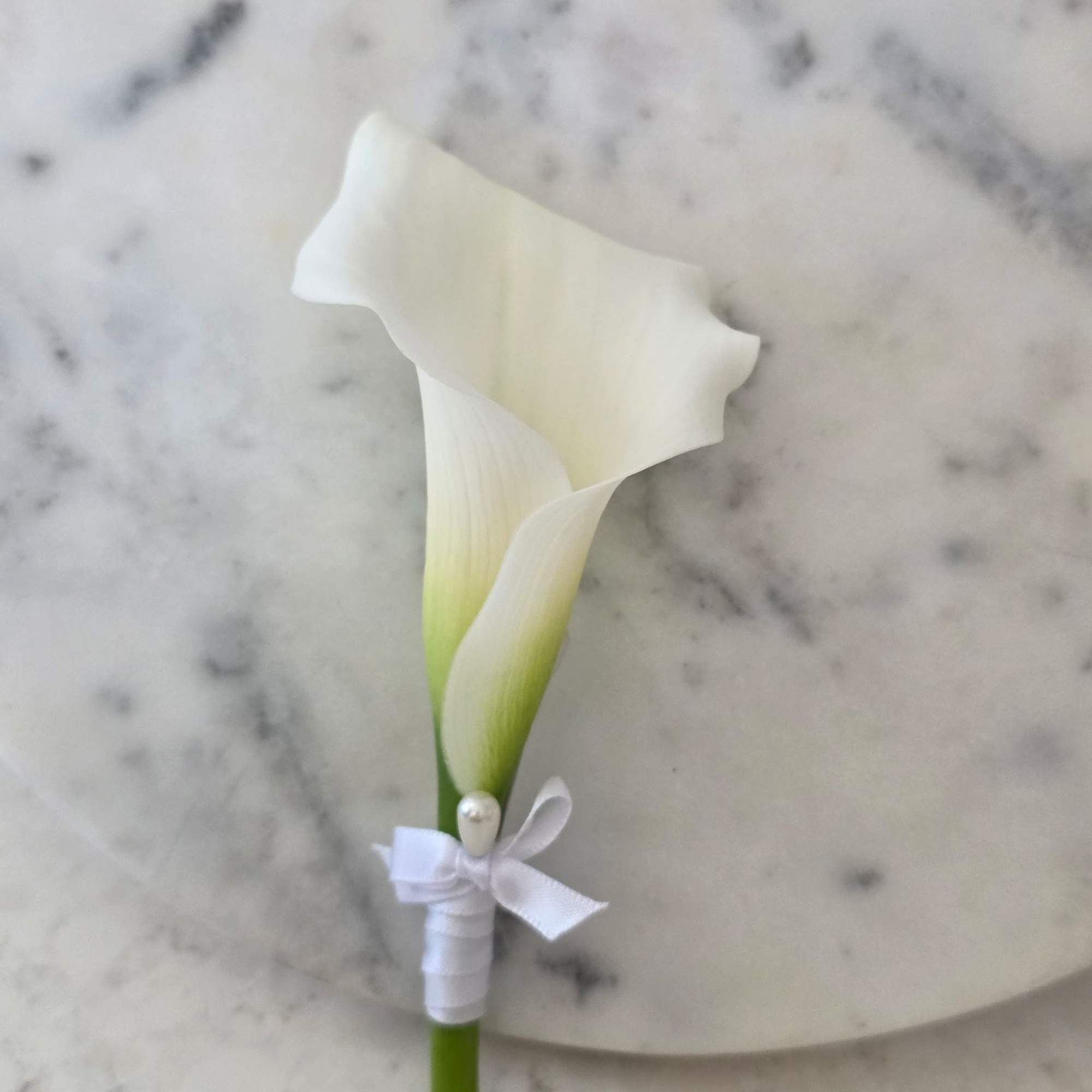 A single soft-white calla lily boutonniere with a whisper of green at