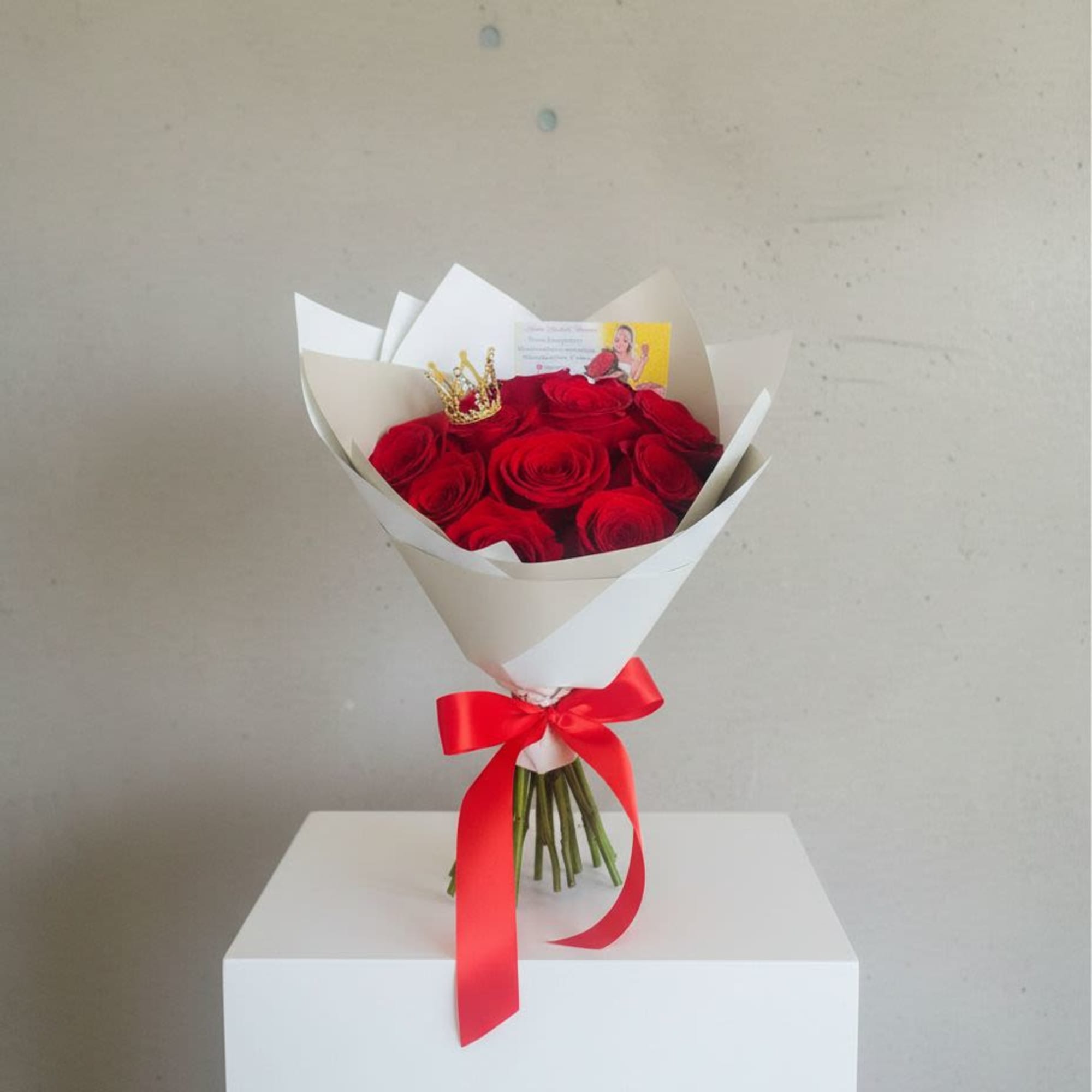 Bouquet of red roses wrapped in white paper with a red ribbon and small crown accent.